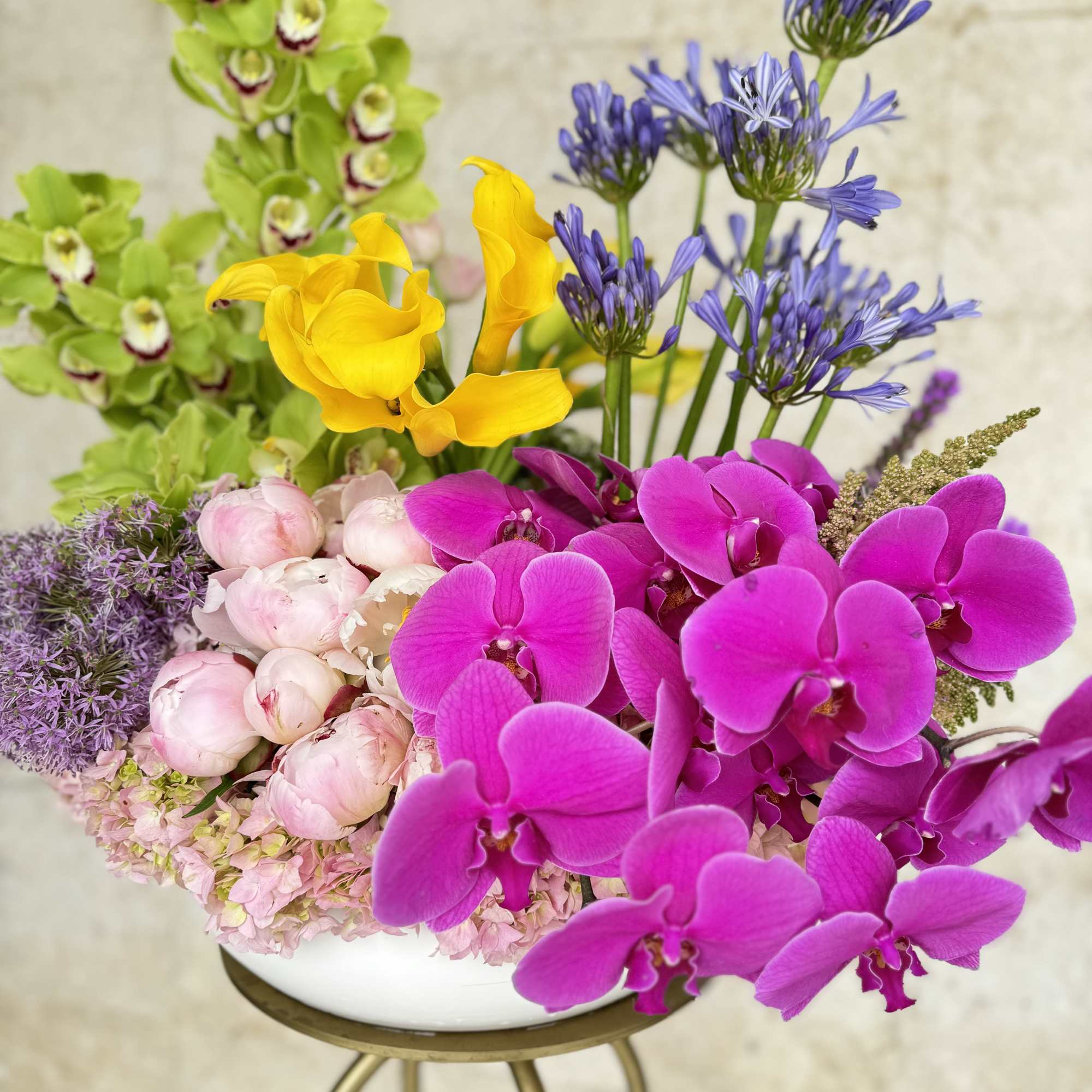 Colorful mixed bouquet with orchids, calla lilies, and peonies in a white bowl vase