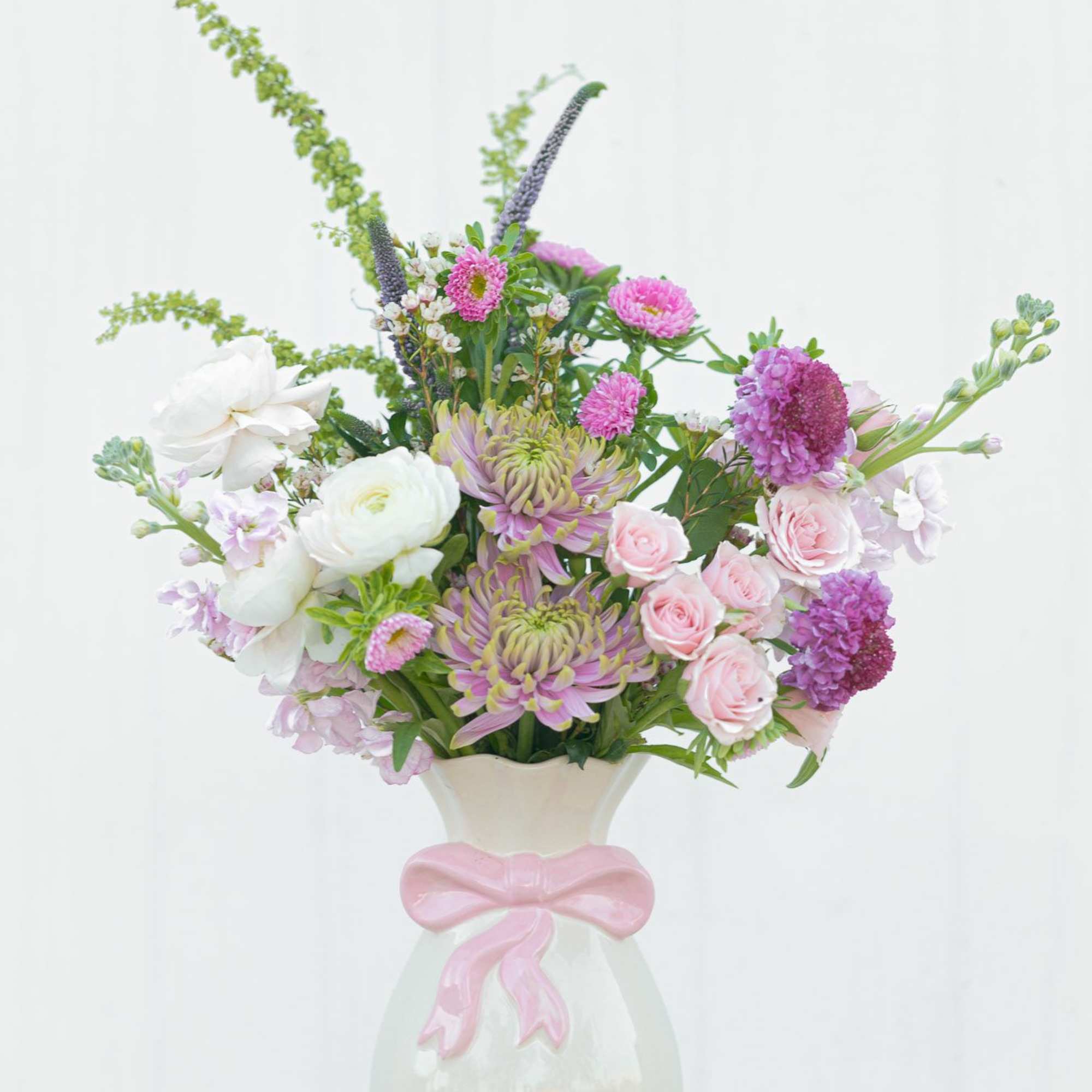 Pink and white mixed flower arrangement in a white vase with a pink bow