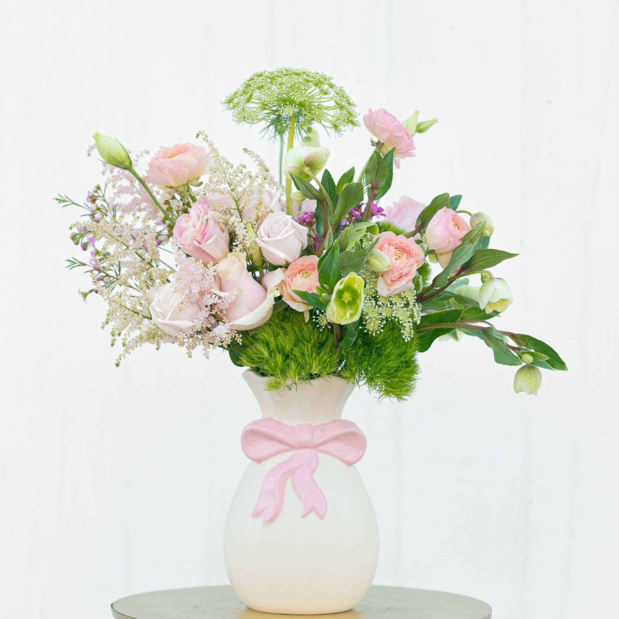 Pink and white floral arrangement in a white vase with a pink ribbon