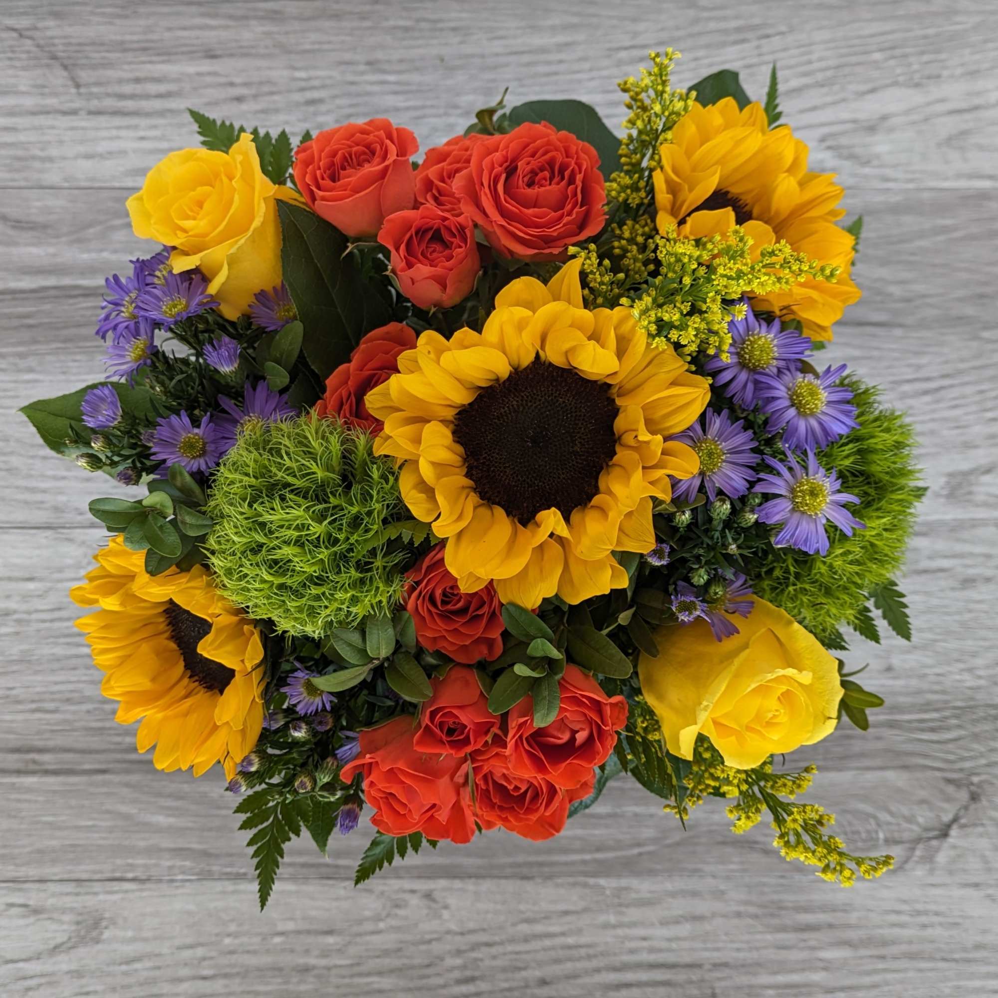 Bouquet of yellow sunflowers, orange and yellow roses, and purple daisies