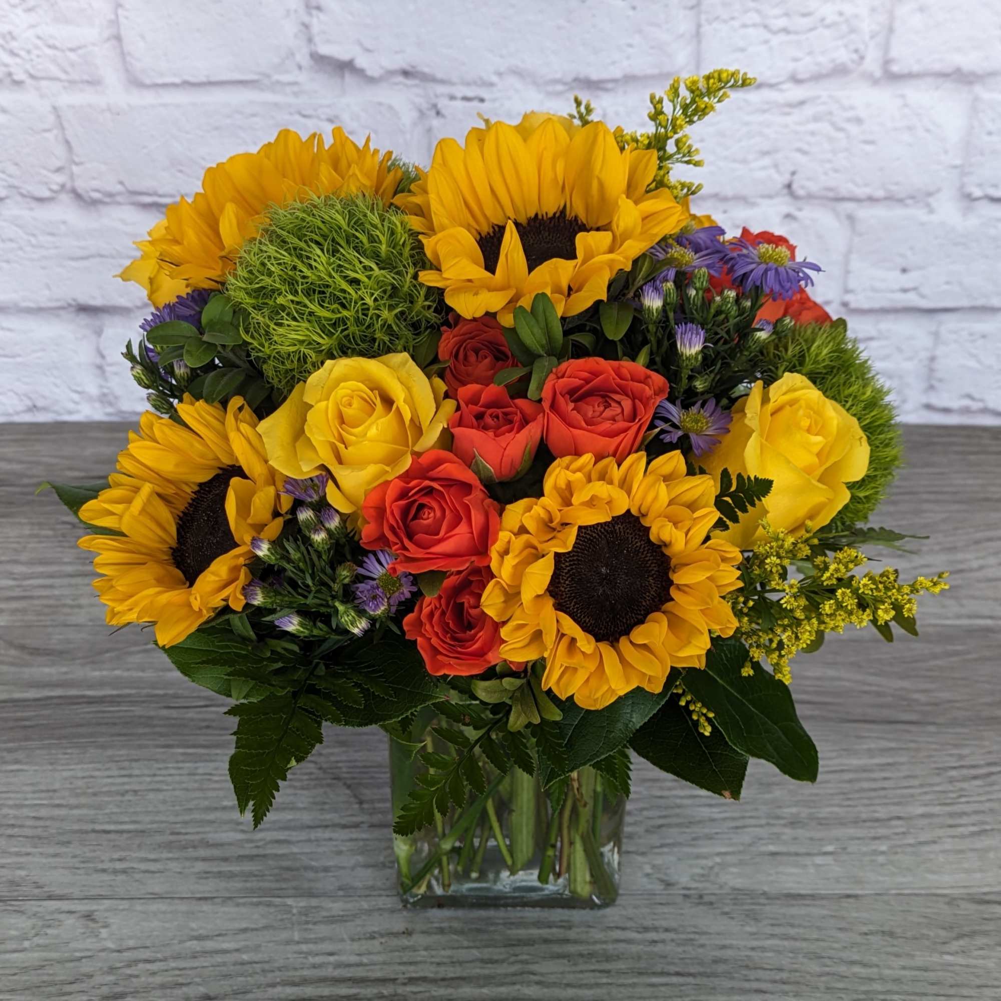 Bouquet of sunflowers, red and yellow roses in a glass vase