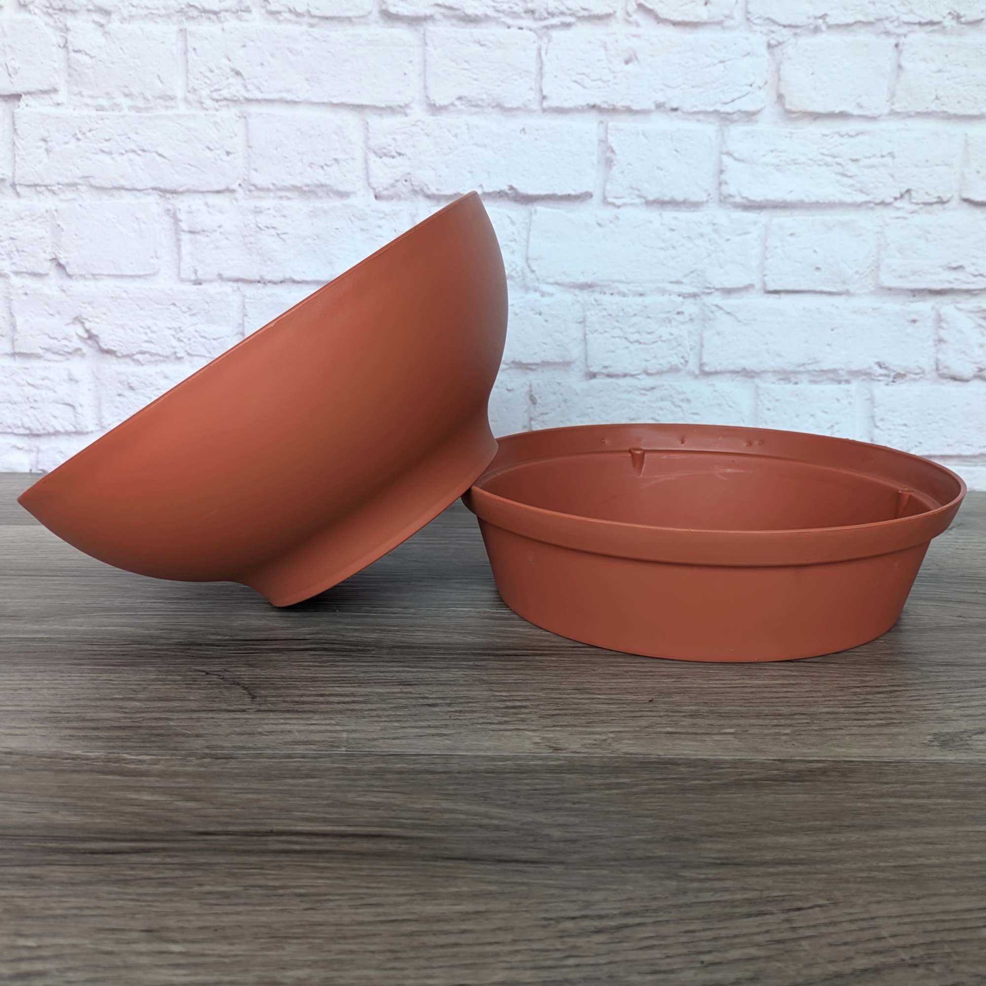 Two terracotta-colored plastic plant pots on a tabletop