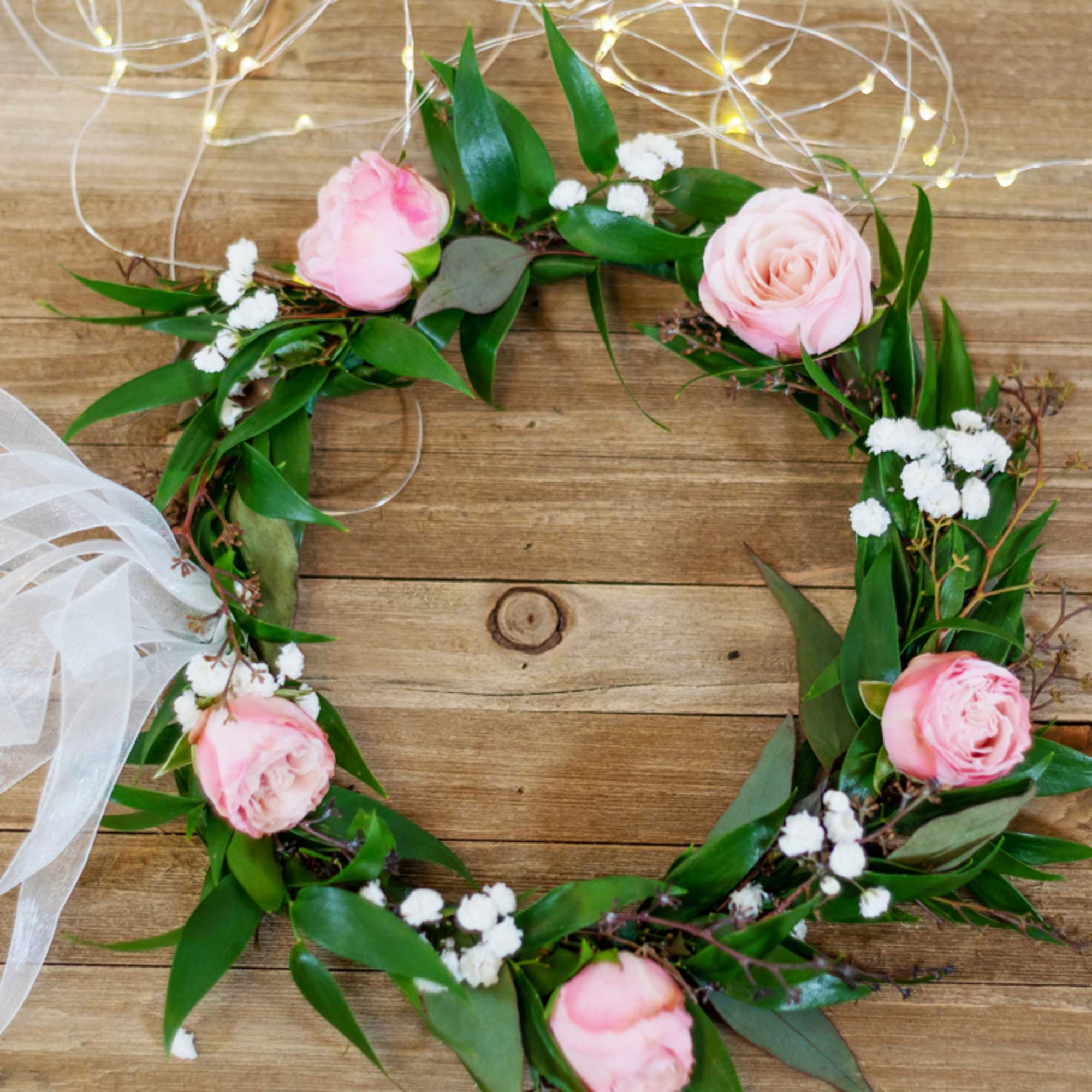 Pink roses arranged in a circular floral wreath with white ribbon.