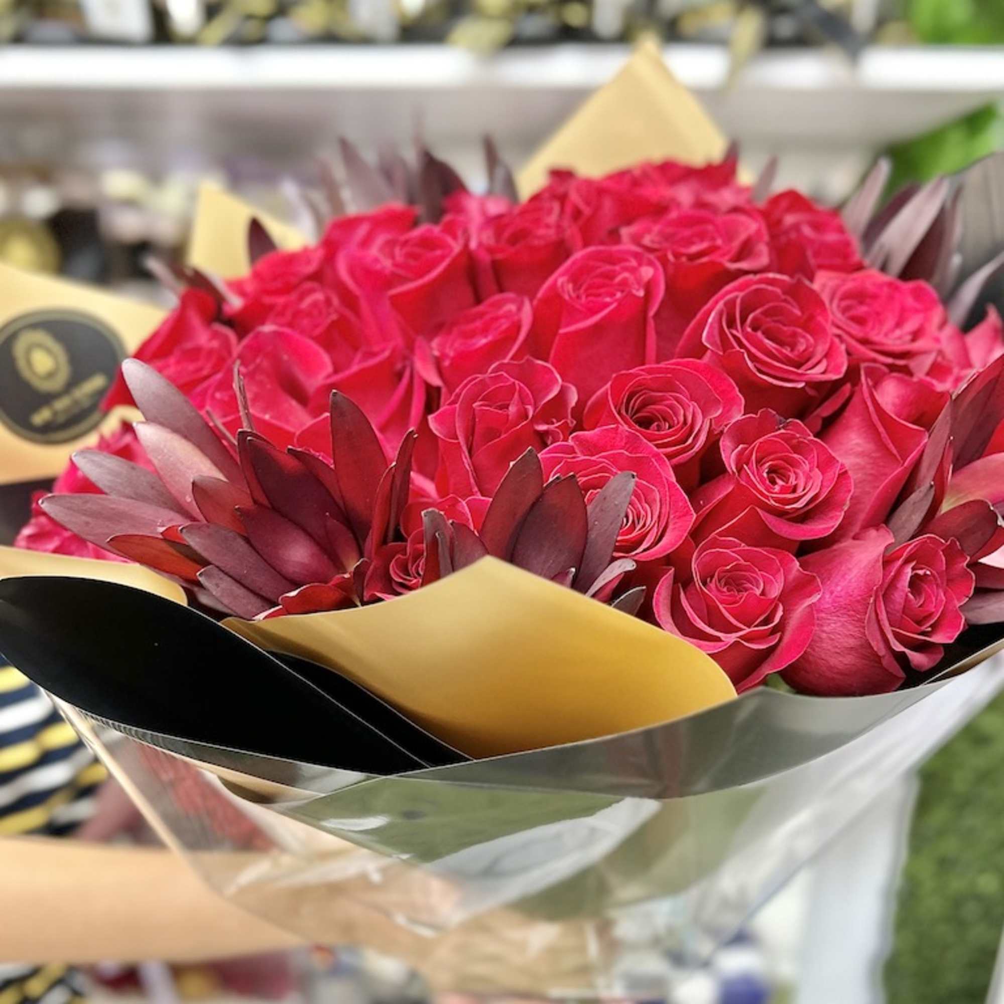 Hand-tied bouquet of bright red roses with dark accents wrapped in black and gold paper
