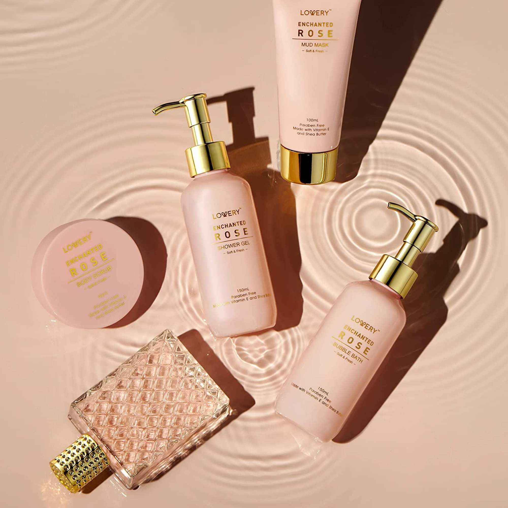 Blush pink rose-scented bath and perfume gift set arranged on a rippled surface.