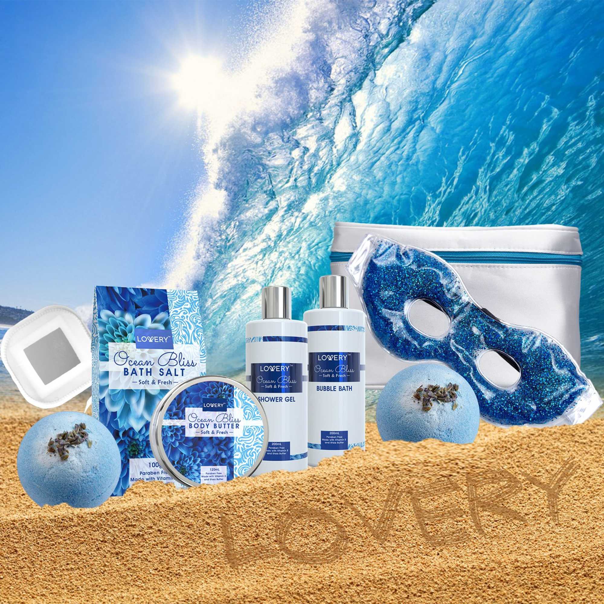 Ocean-themed bath gift set with blue spa products on sand before a crashing wave.