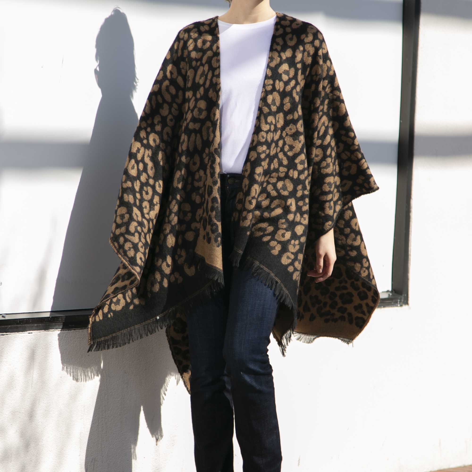 Person wearing a leopard print poncho, white top, jeans, and black boots standing outdoors