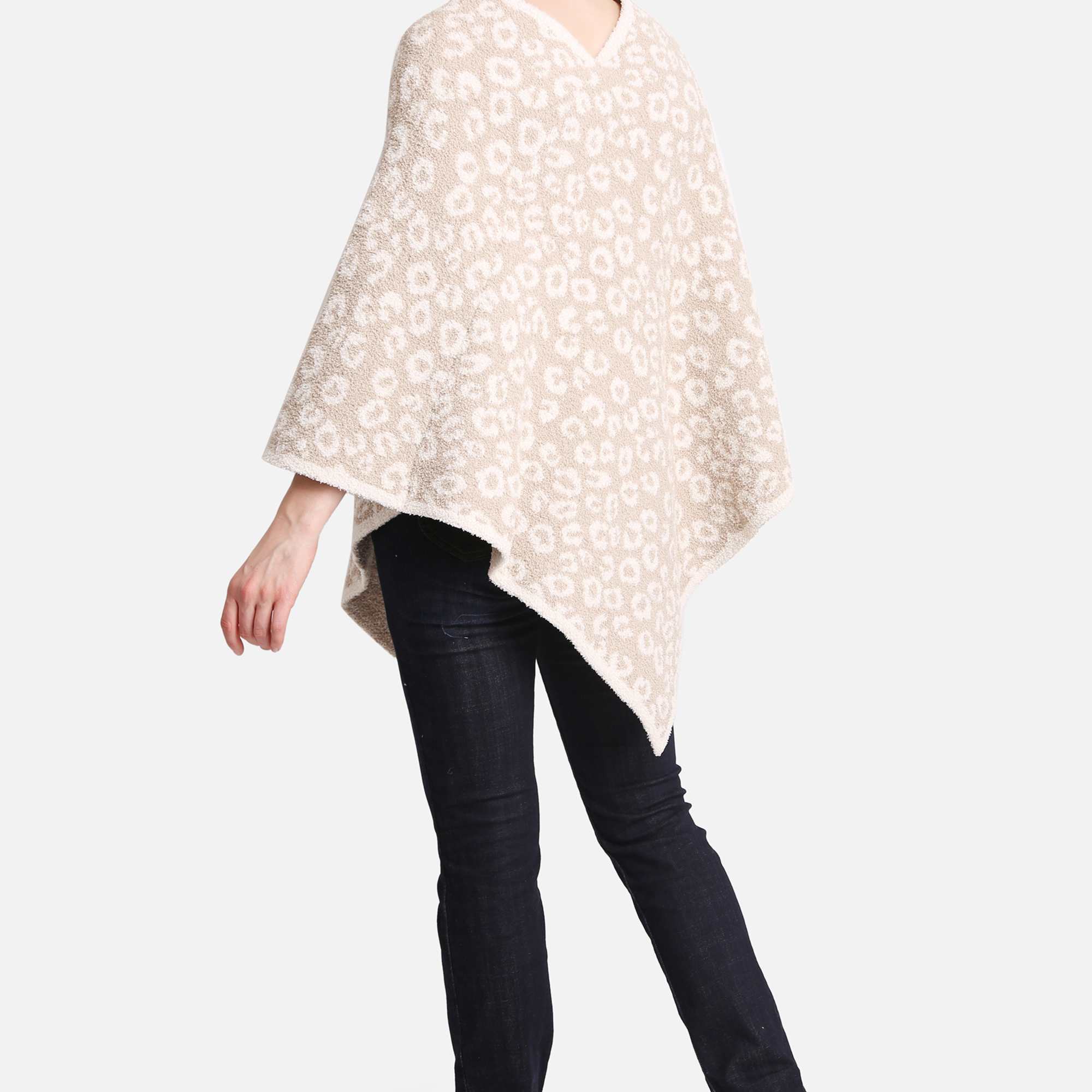 Person wearing a beige patterned poncho with dark jeans and black heeled boots, shown from the back.