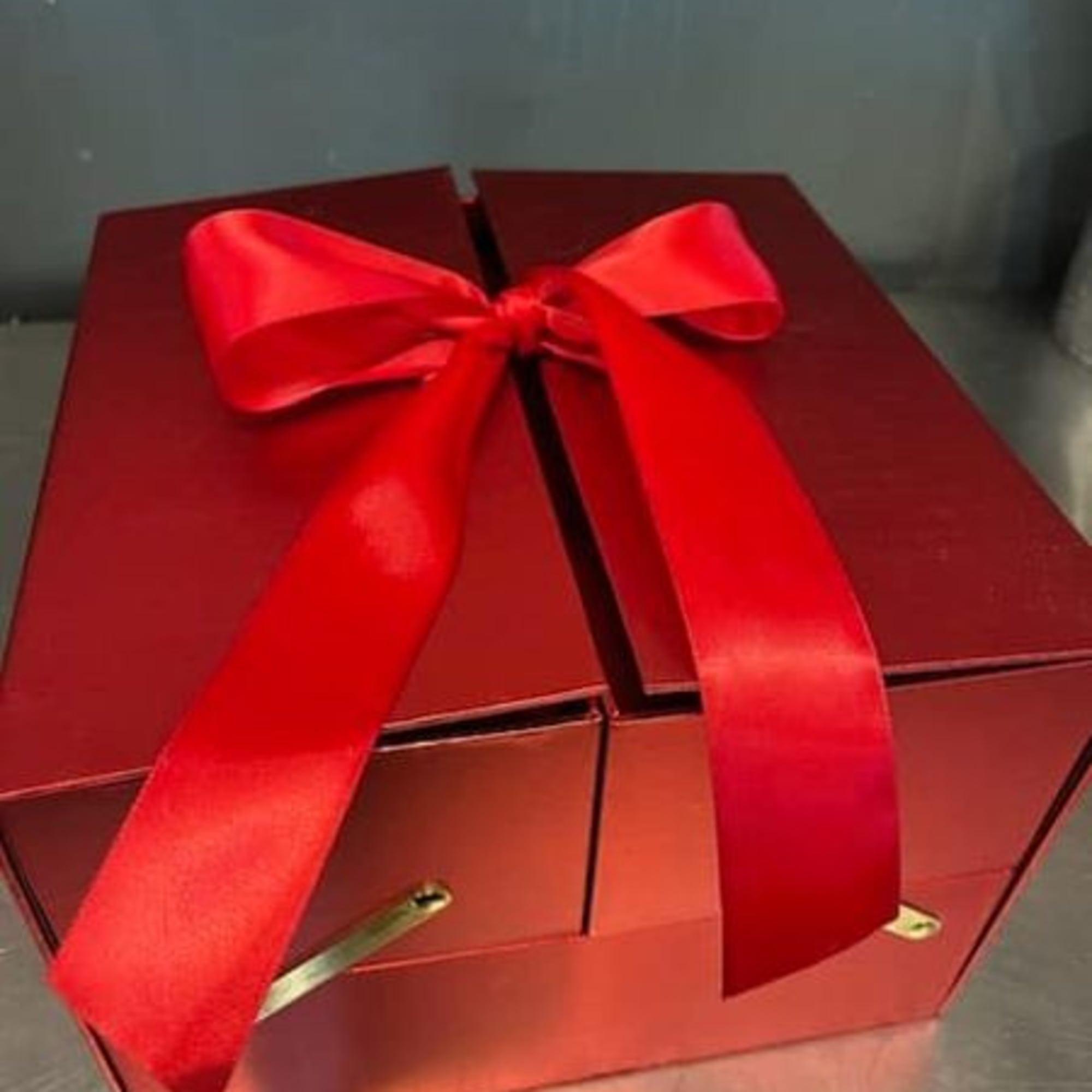 Red gift box with a shiny red bow and gold accents on a reflective surface