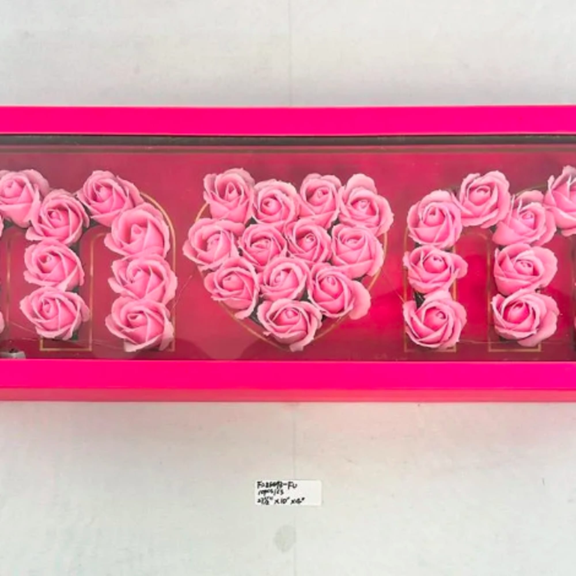 Bright pink boxed arrangement of artificial pink roses spelling MOM with a heart center