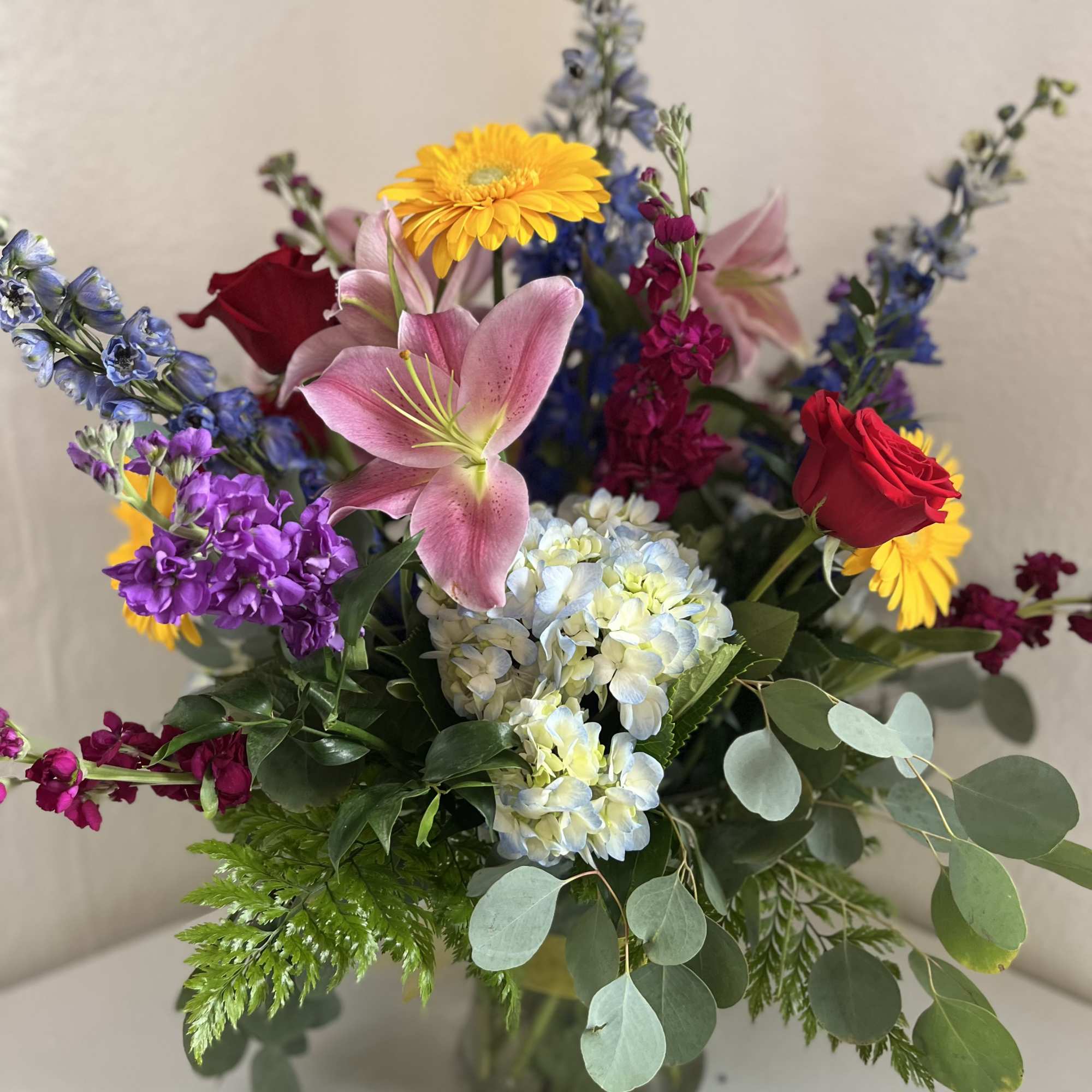 Mixed bouquet with pink lilies, red roses, and yellow daisies in a glass vase