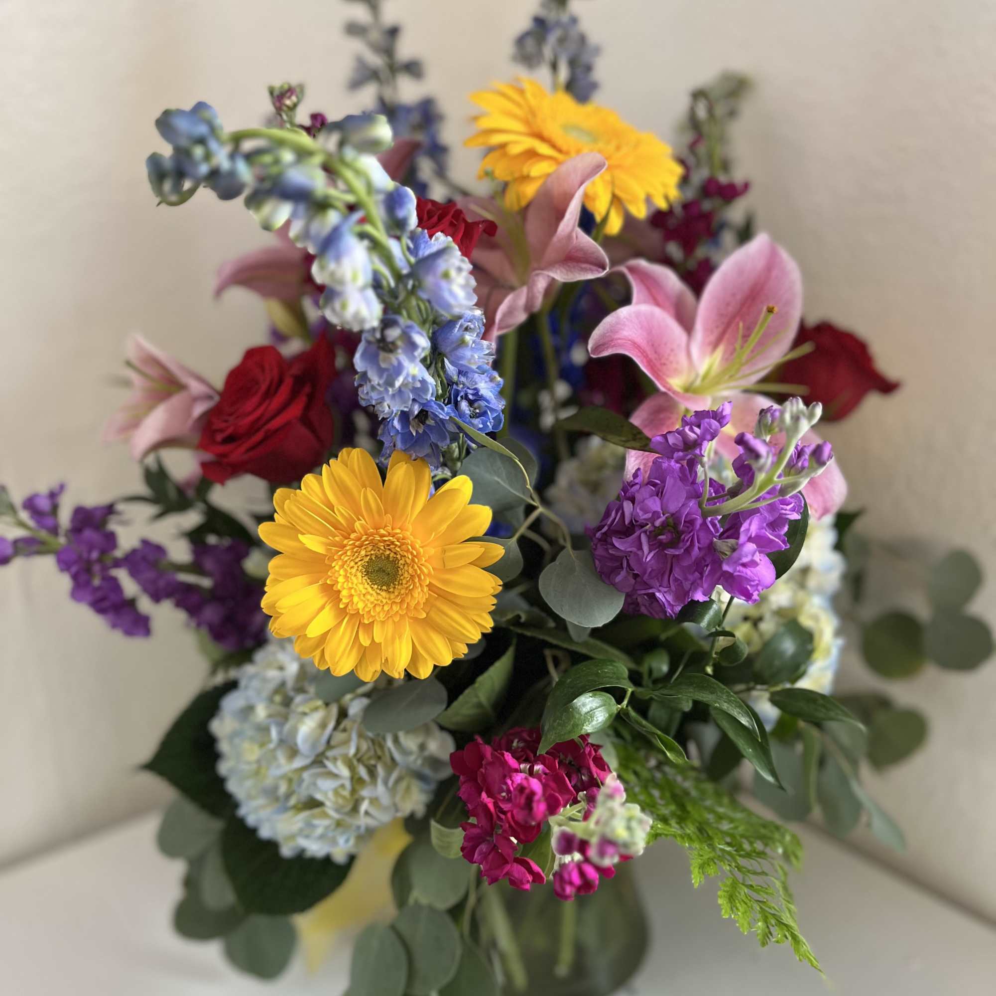 Mixed bouquet with yellow gerbera daisies, pink lilies, and purple flowers in a glass vase