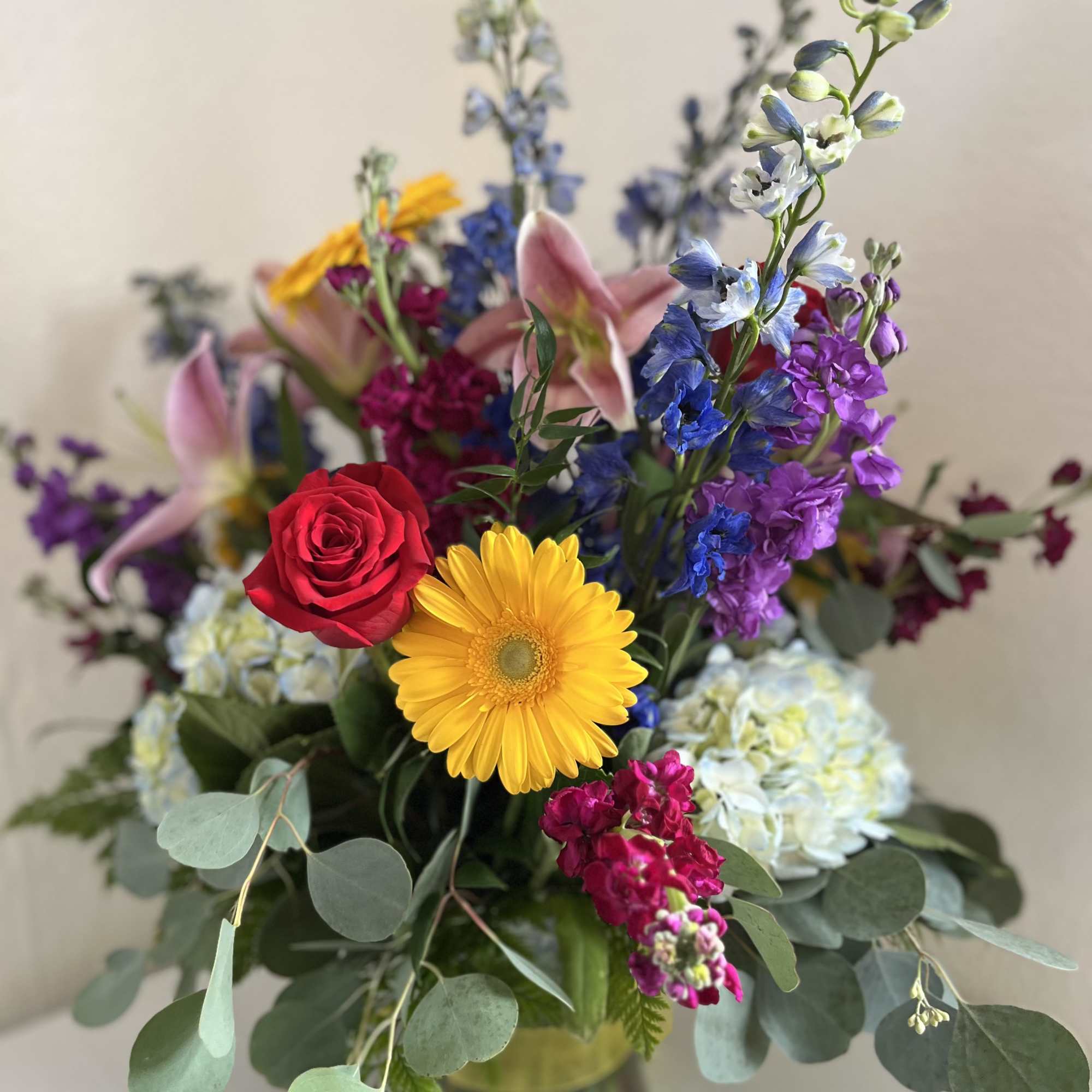 Mixed bouquet with a red rose, yellow gerbera daisy, and purple blooms in a glass vase