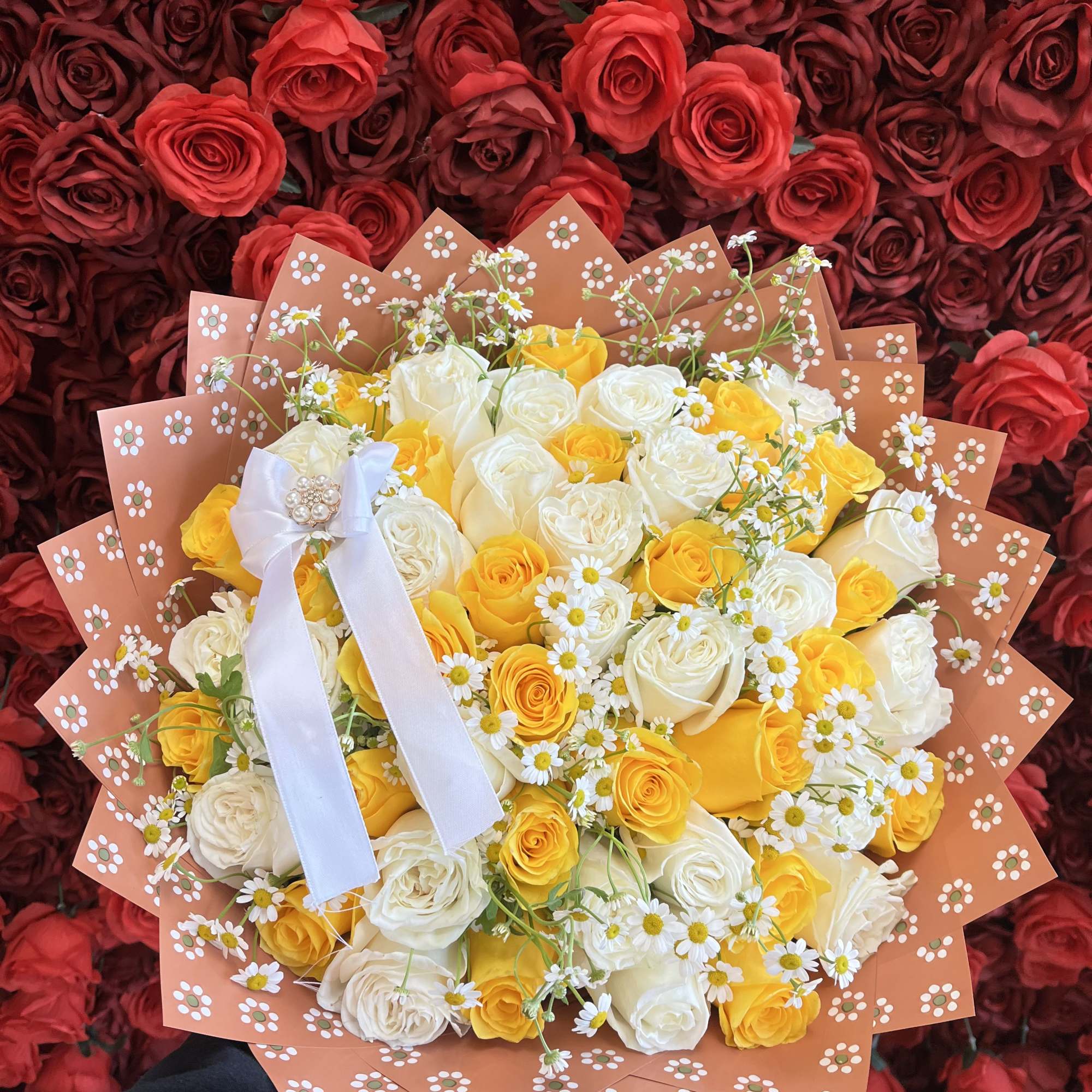 Bouquet of yellow and white roses with small daisies in peach wrap