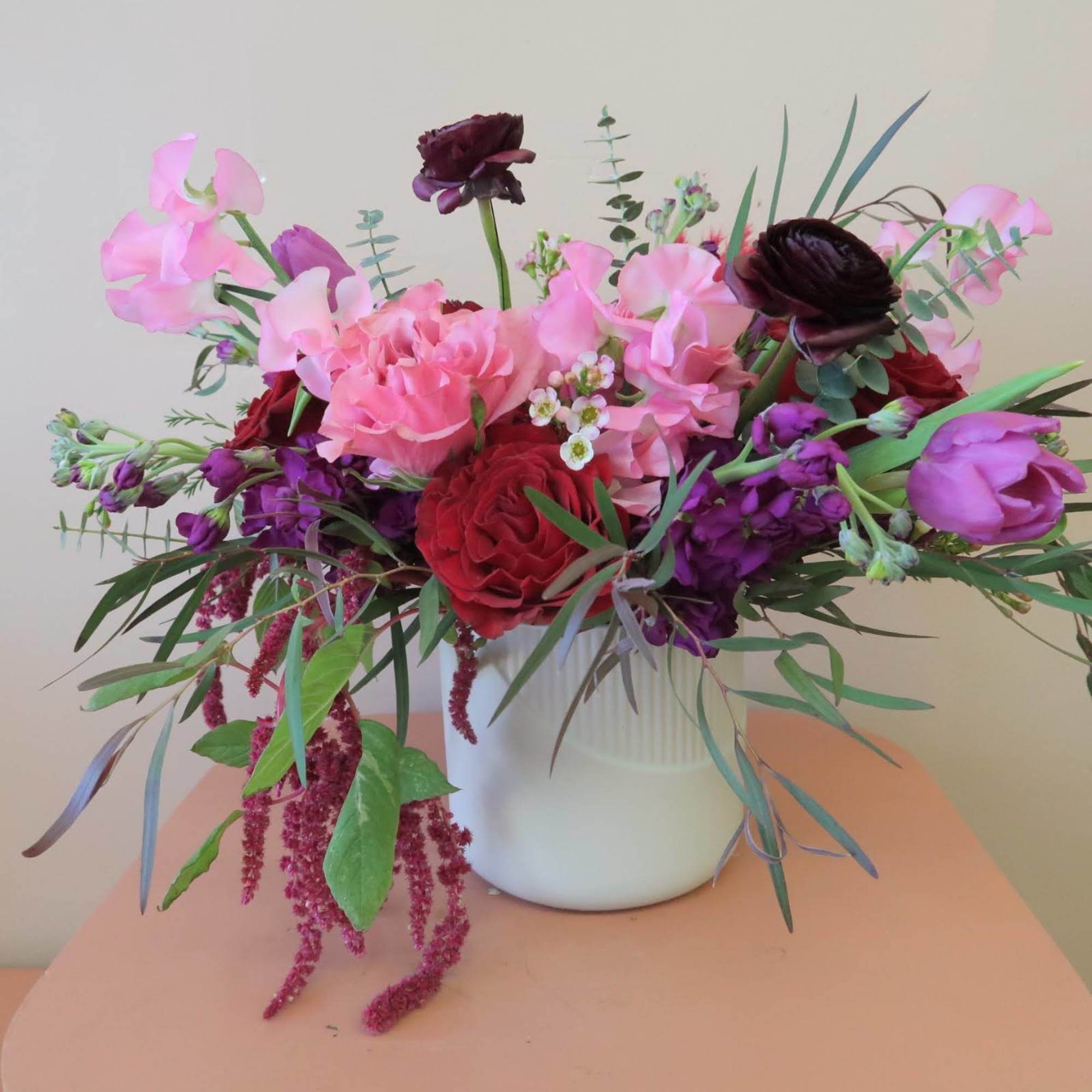 Mixed bouquet of pink, red, and purple flowers in a white vase