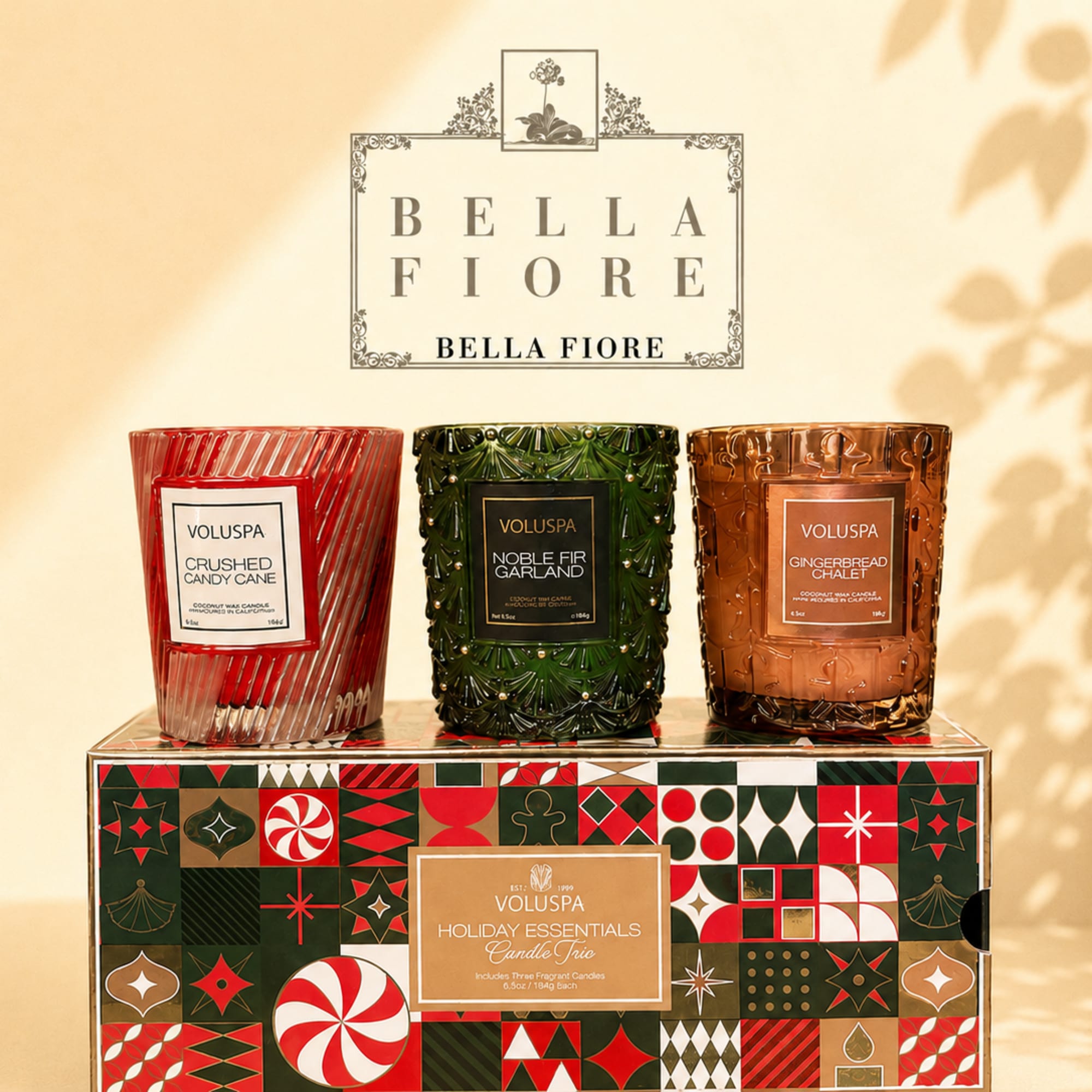 Three holiday candles in red, green, and amber glass jars on a decorated box
