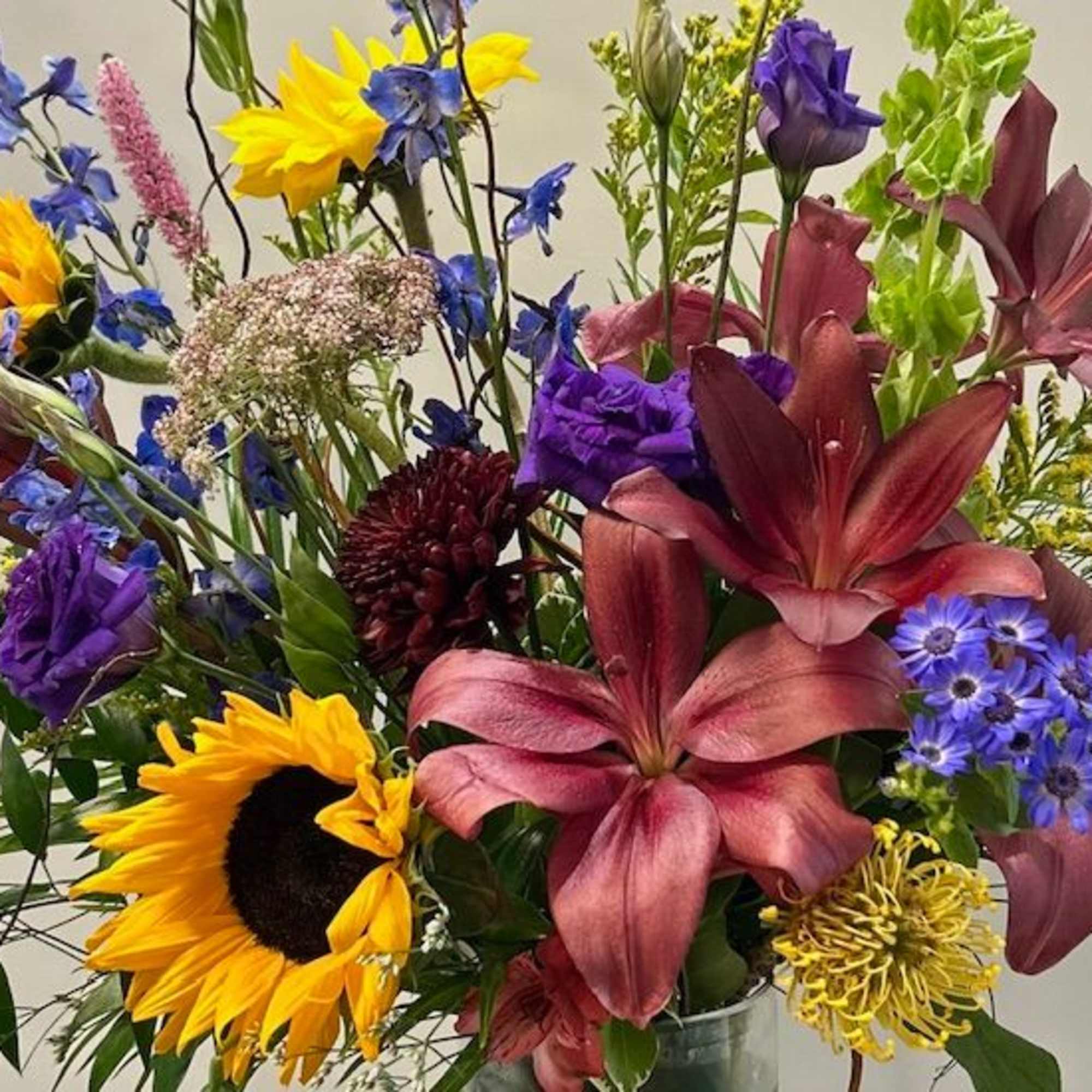 Mixed bouquet with sunflowers, lilies, and purple blooms in a vase