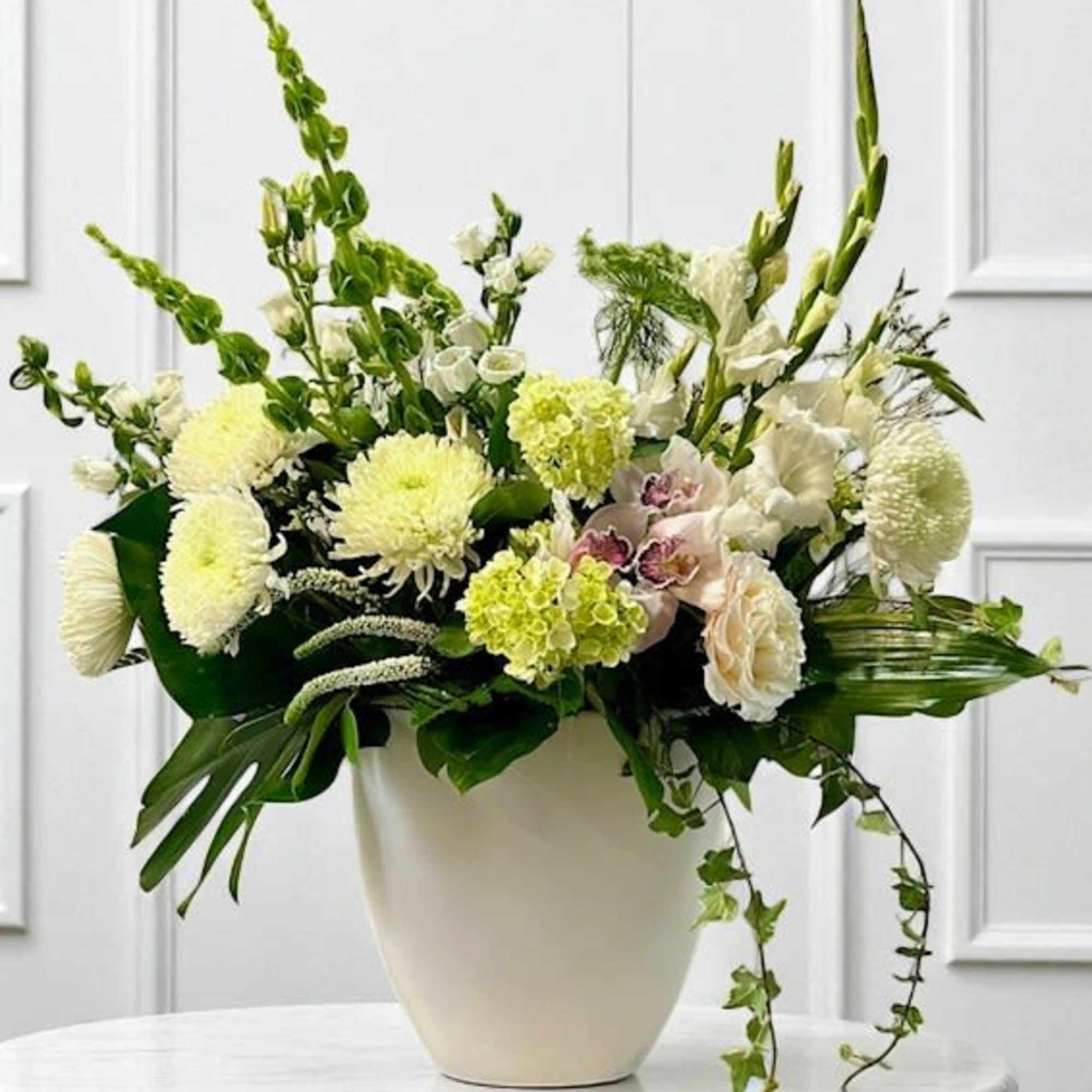 White floral arrangement in a cream vase with tall green stems