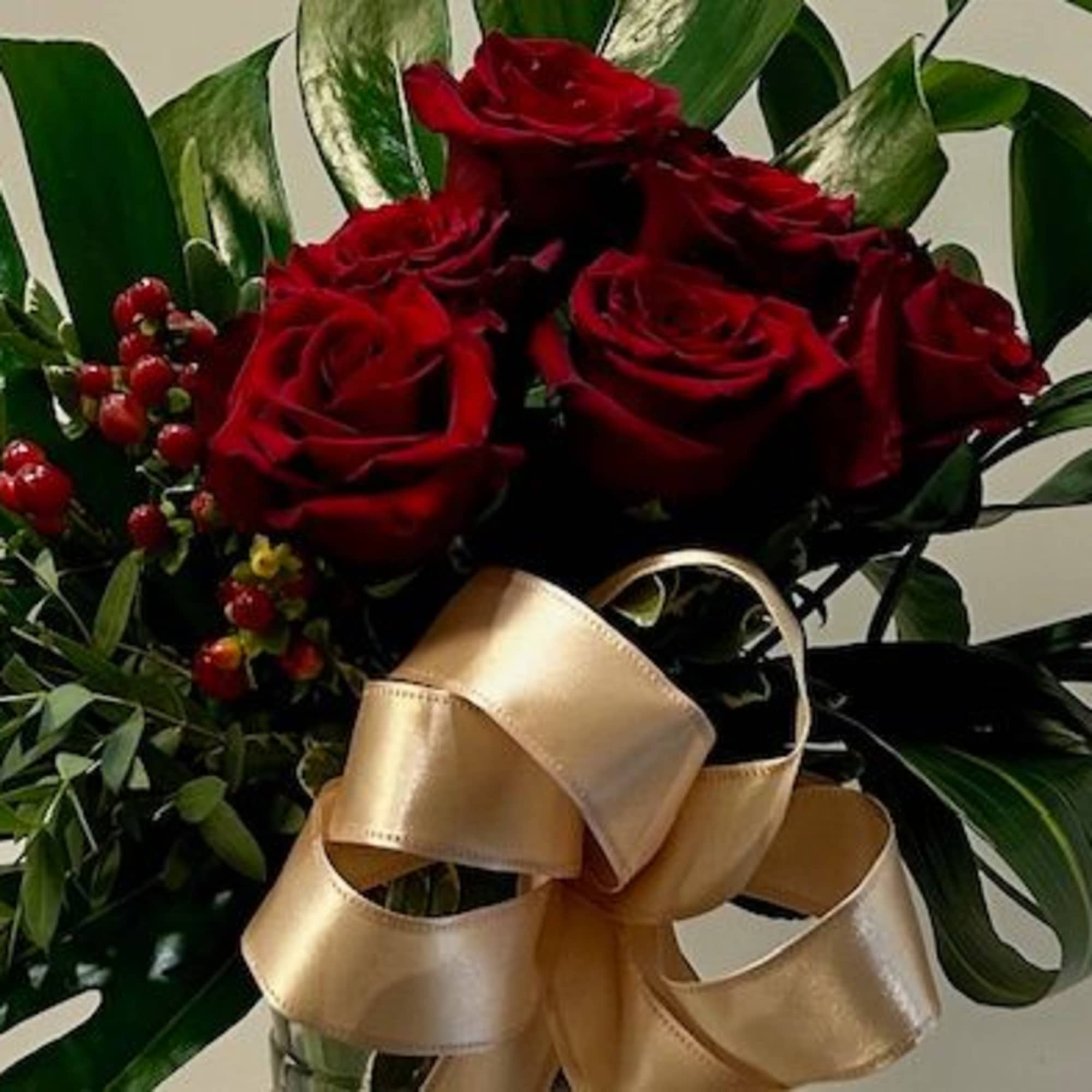 Compact arrangement of red roses with tropical foliage and a gold ribbon bow in a clear glass vase