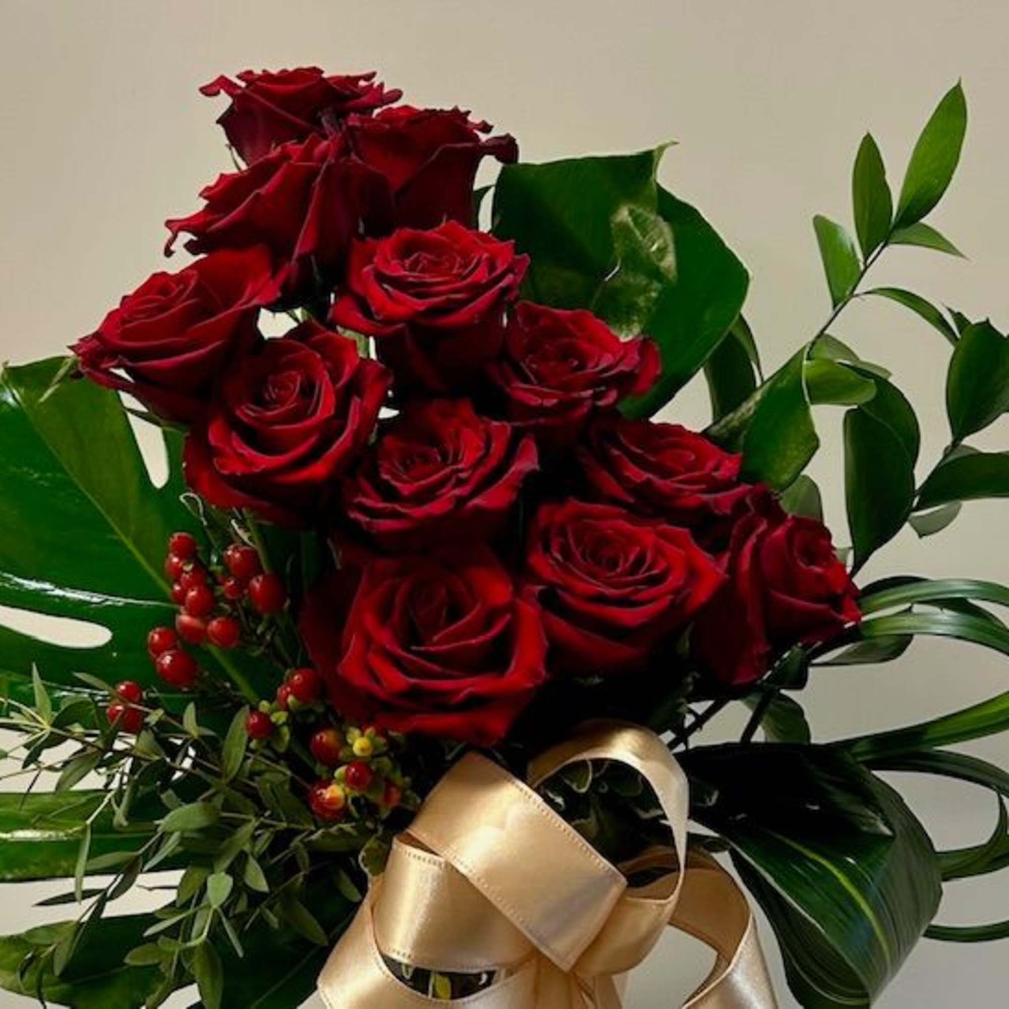 Arrangement of red roses with large tropical green leaves and a gold satin bow.
