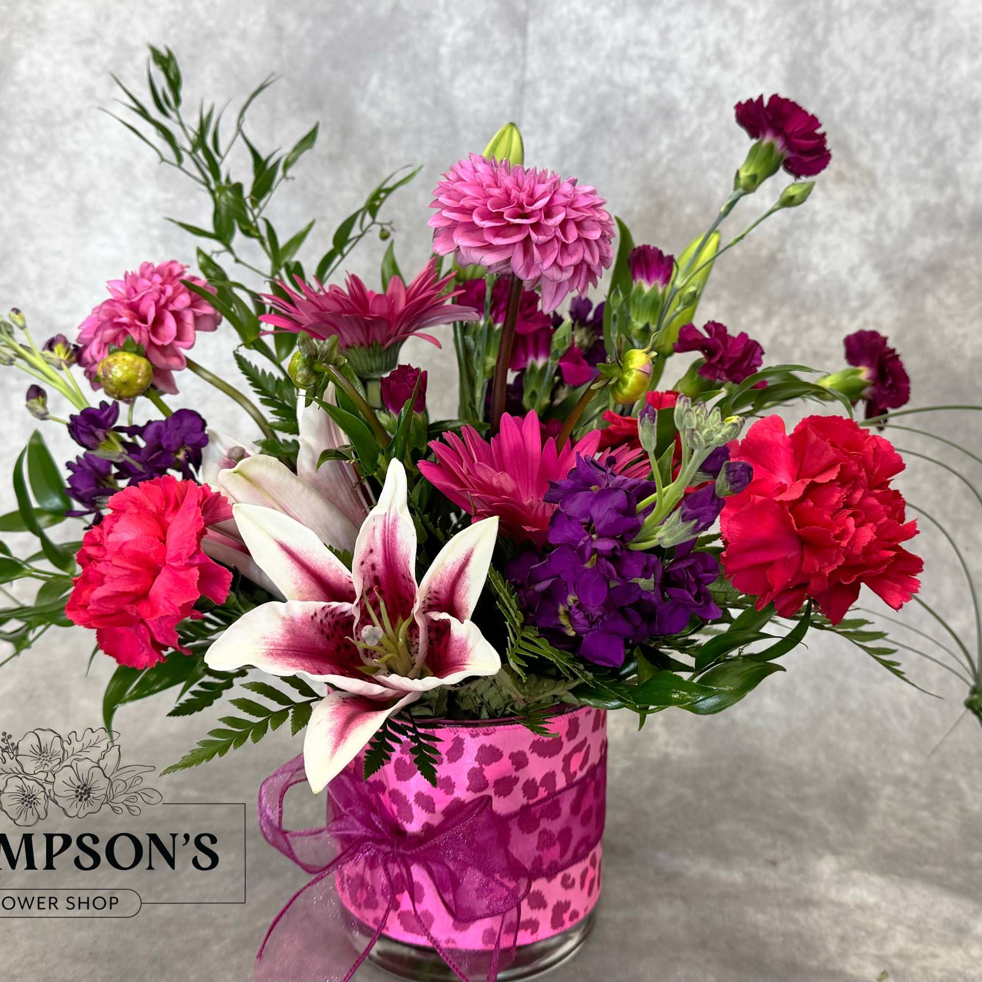 Mixed pink and purple bouquet in a clear glass vase with a ribbon