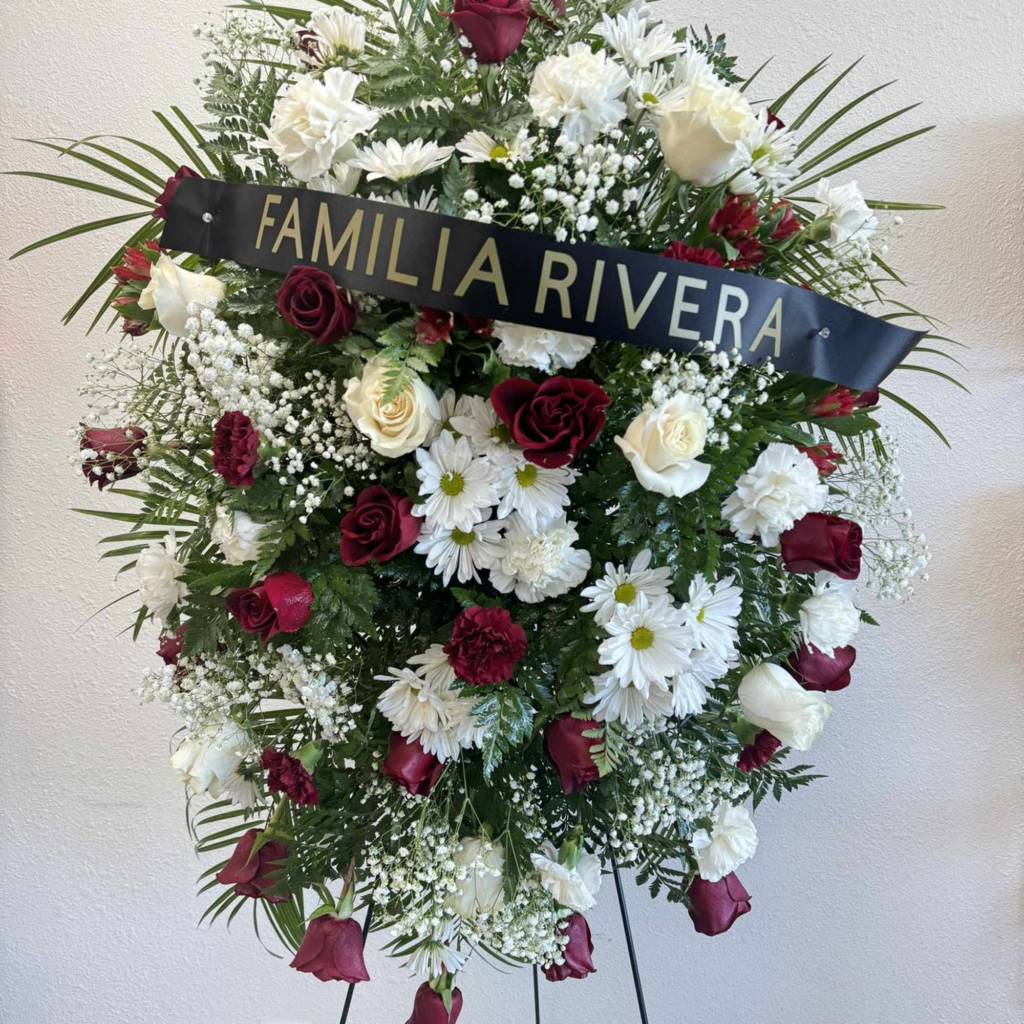 Standing funeral wreath of red and white flowers with a name ribbon