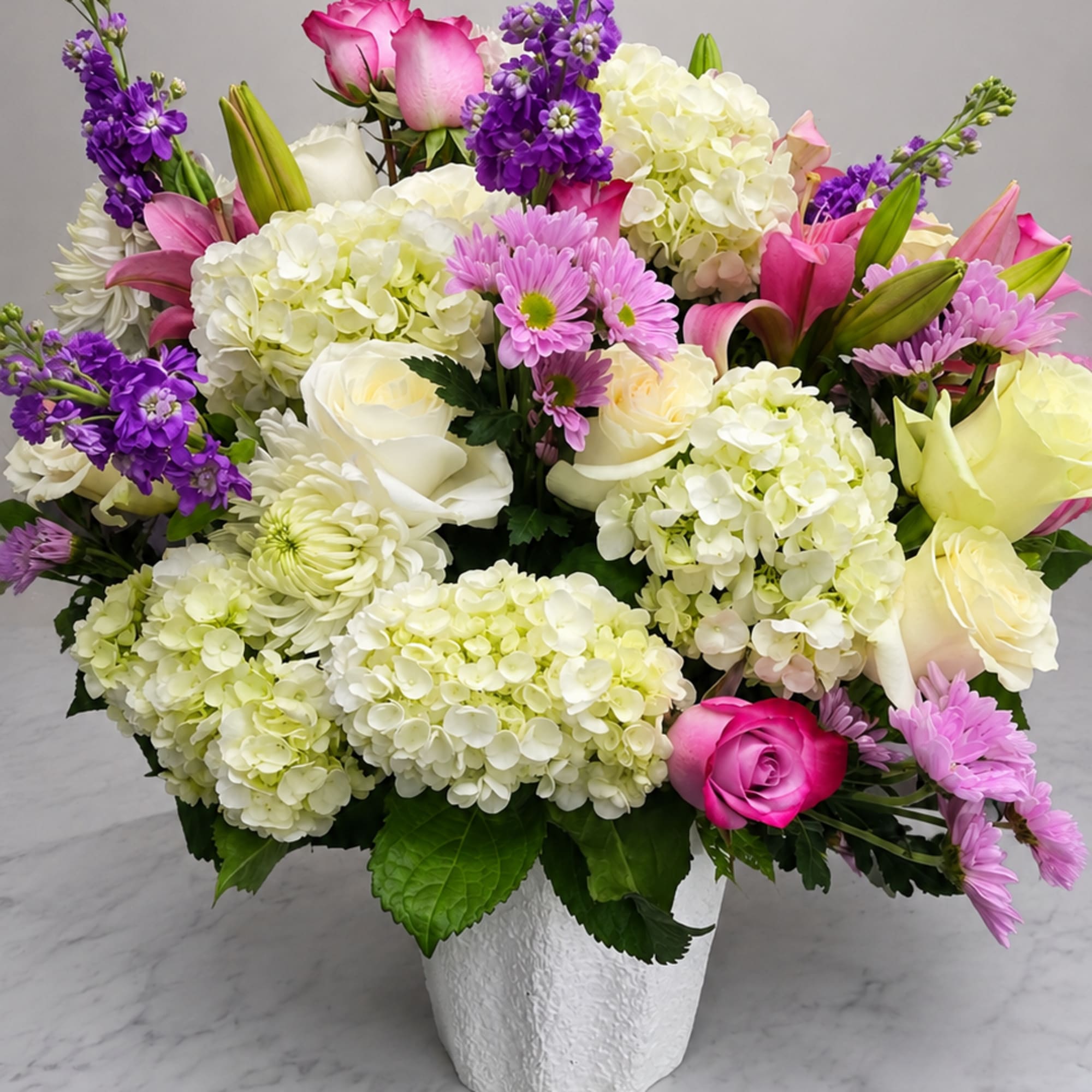 Mixed bouquet of pink, white, and purple flowers in a white vase