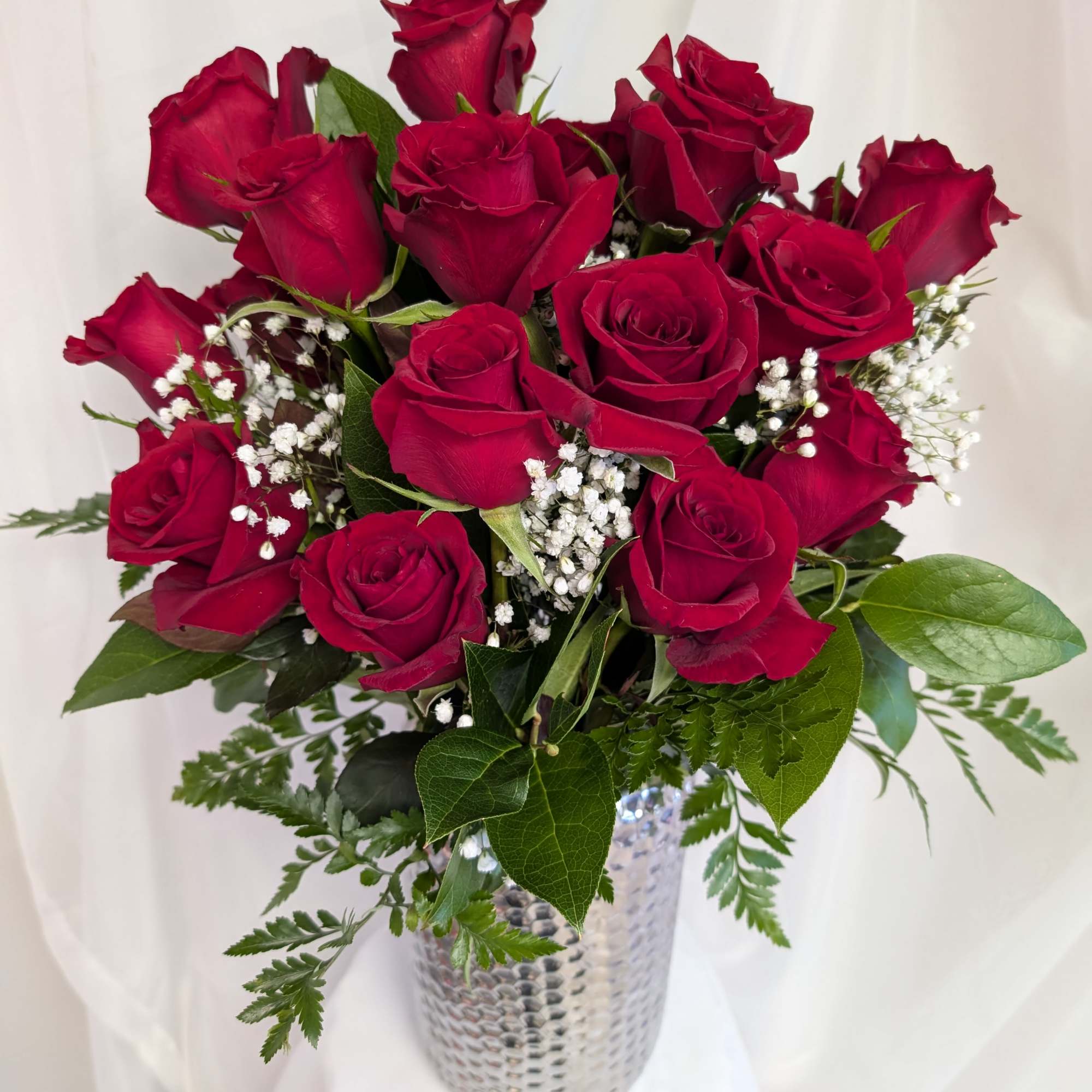 Red roses arranged in a silver vase with baby's breath