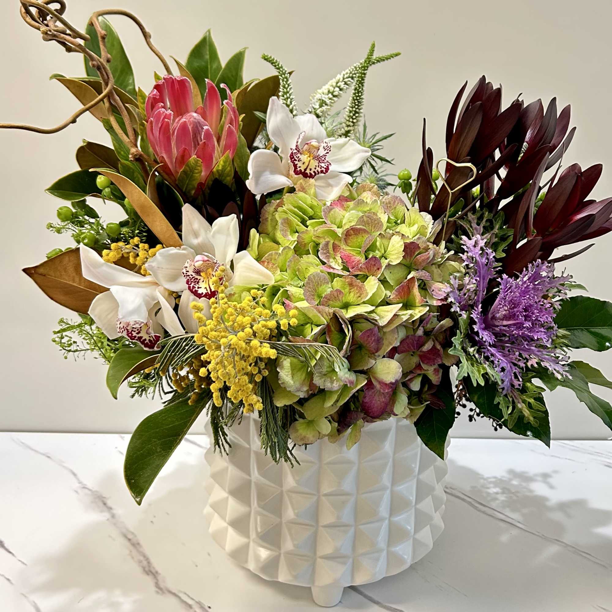 Mixed floral arrangement in a white textured vase with pink, white, green, and purple blooms