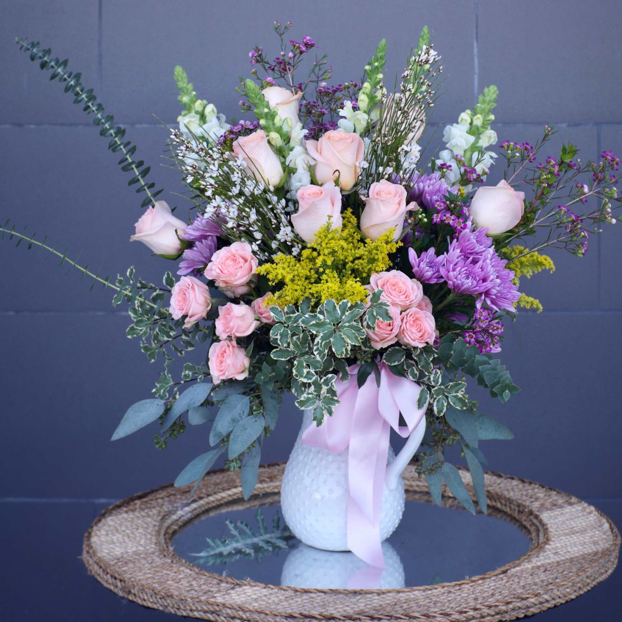 Pink roses and purple flowers arranged in a white vase with a ribbon