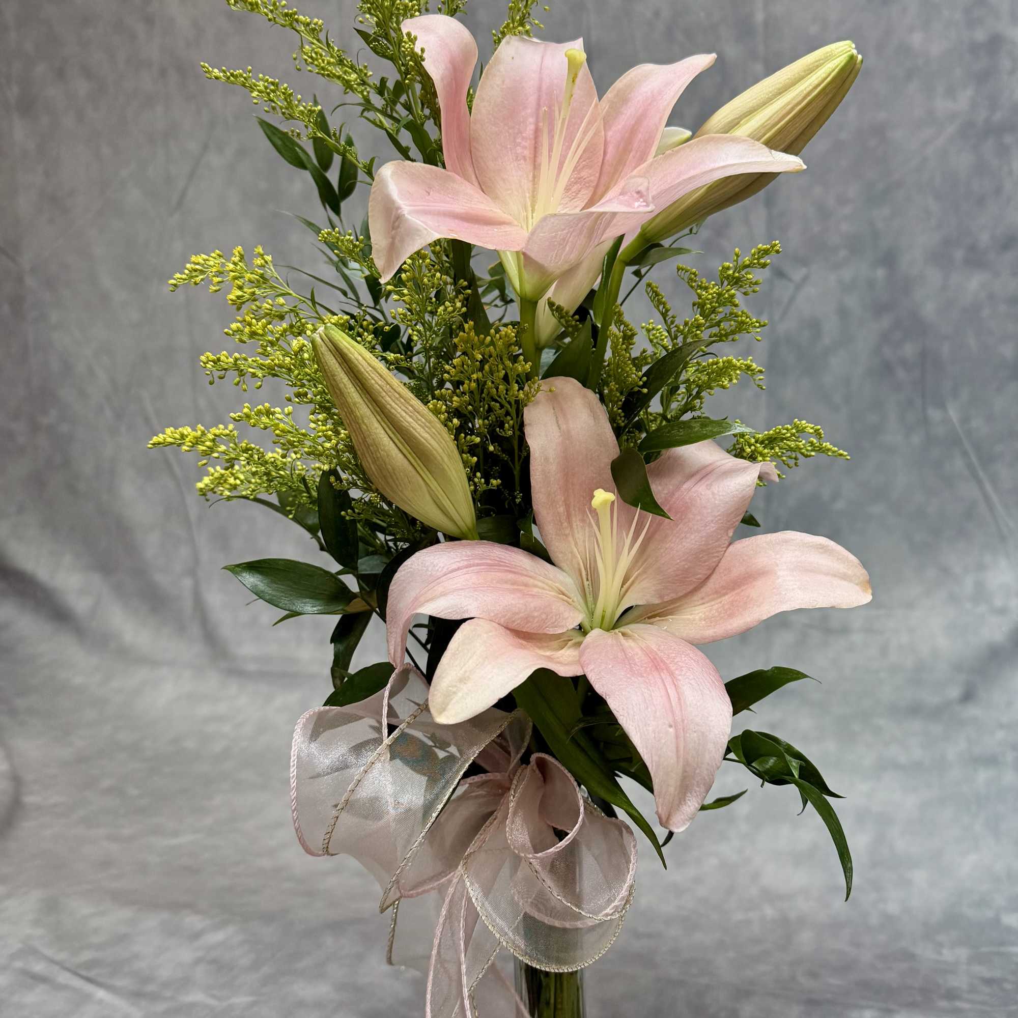Pink lilies in a glass vase with a ribbon bow