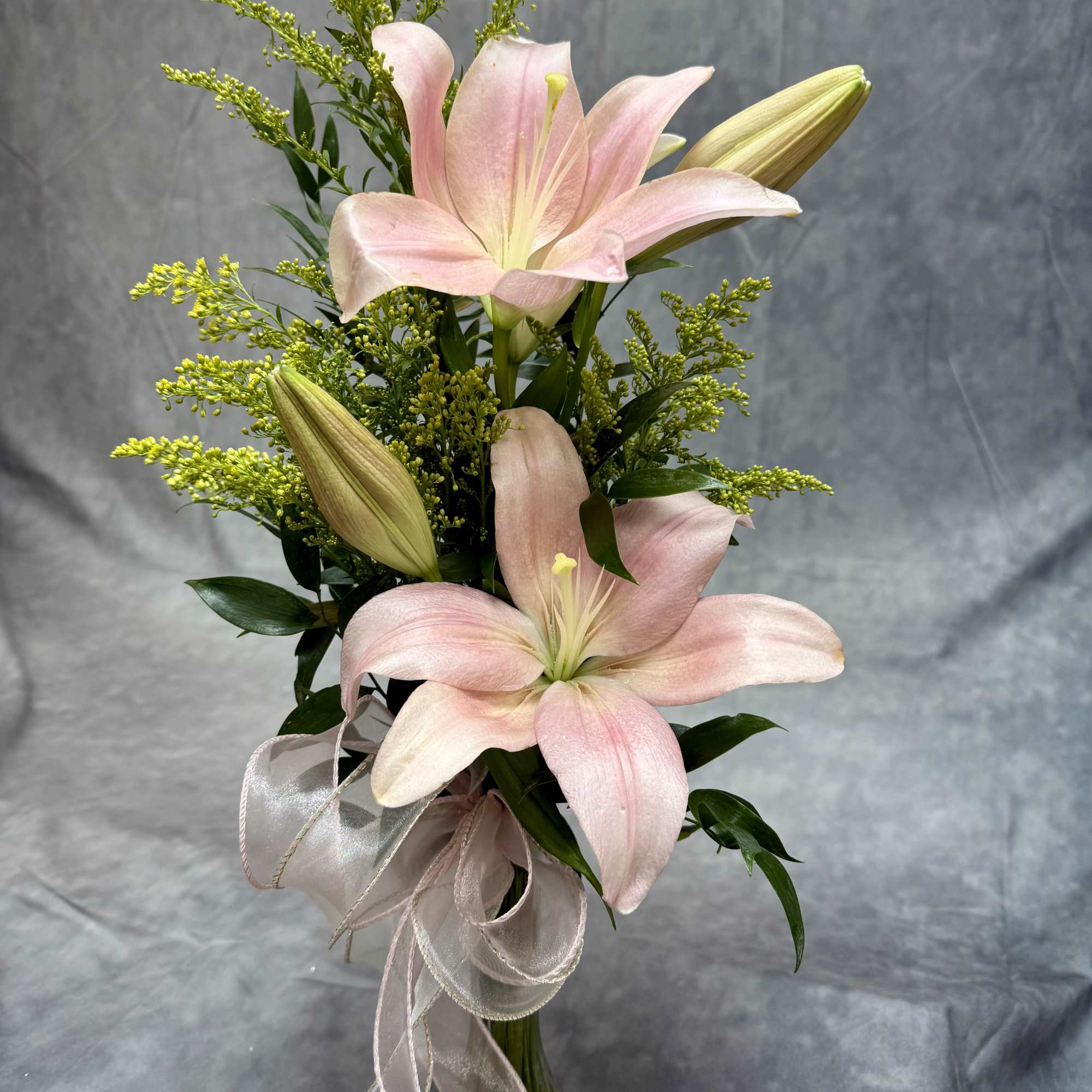 Pink lilies arranged in a clear vase with a ribbon bow
