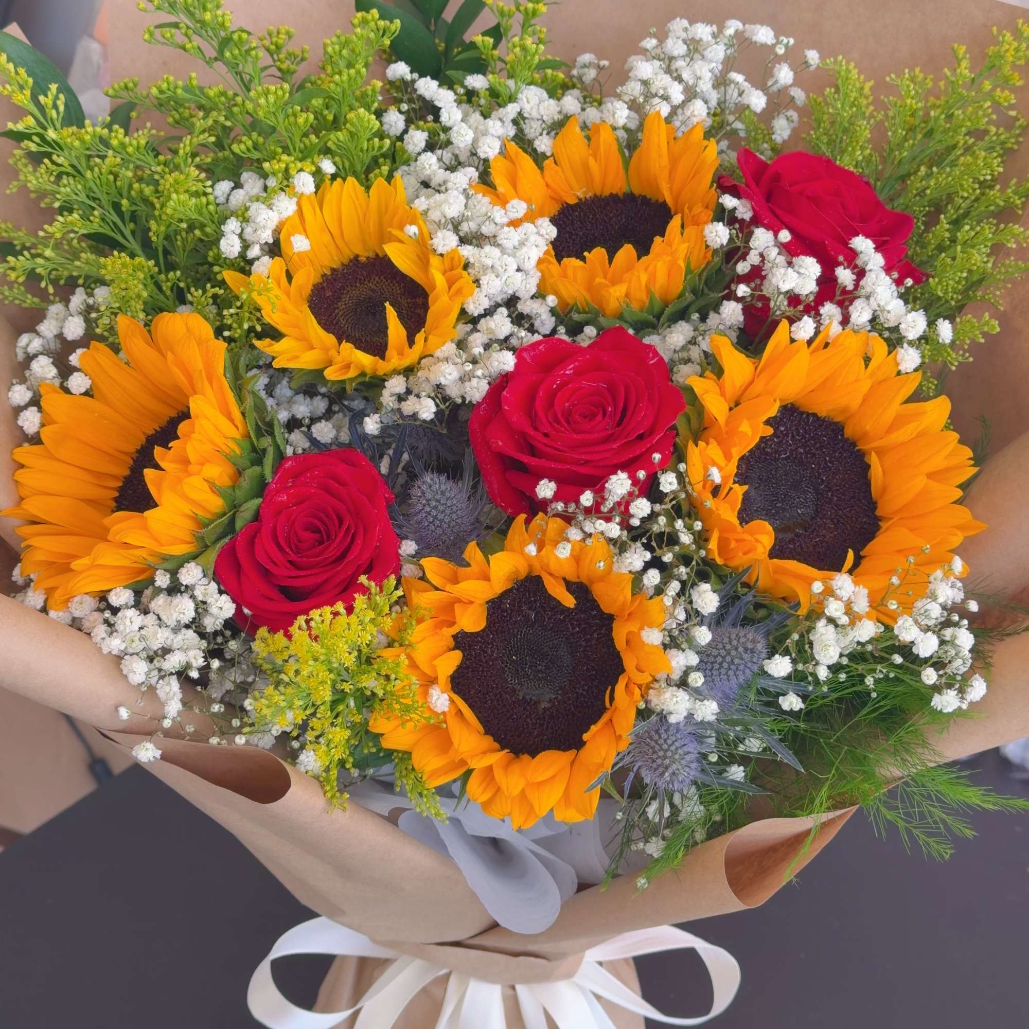 Bouquet of sunflowers and red roses wrapped in brown paper