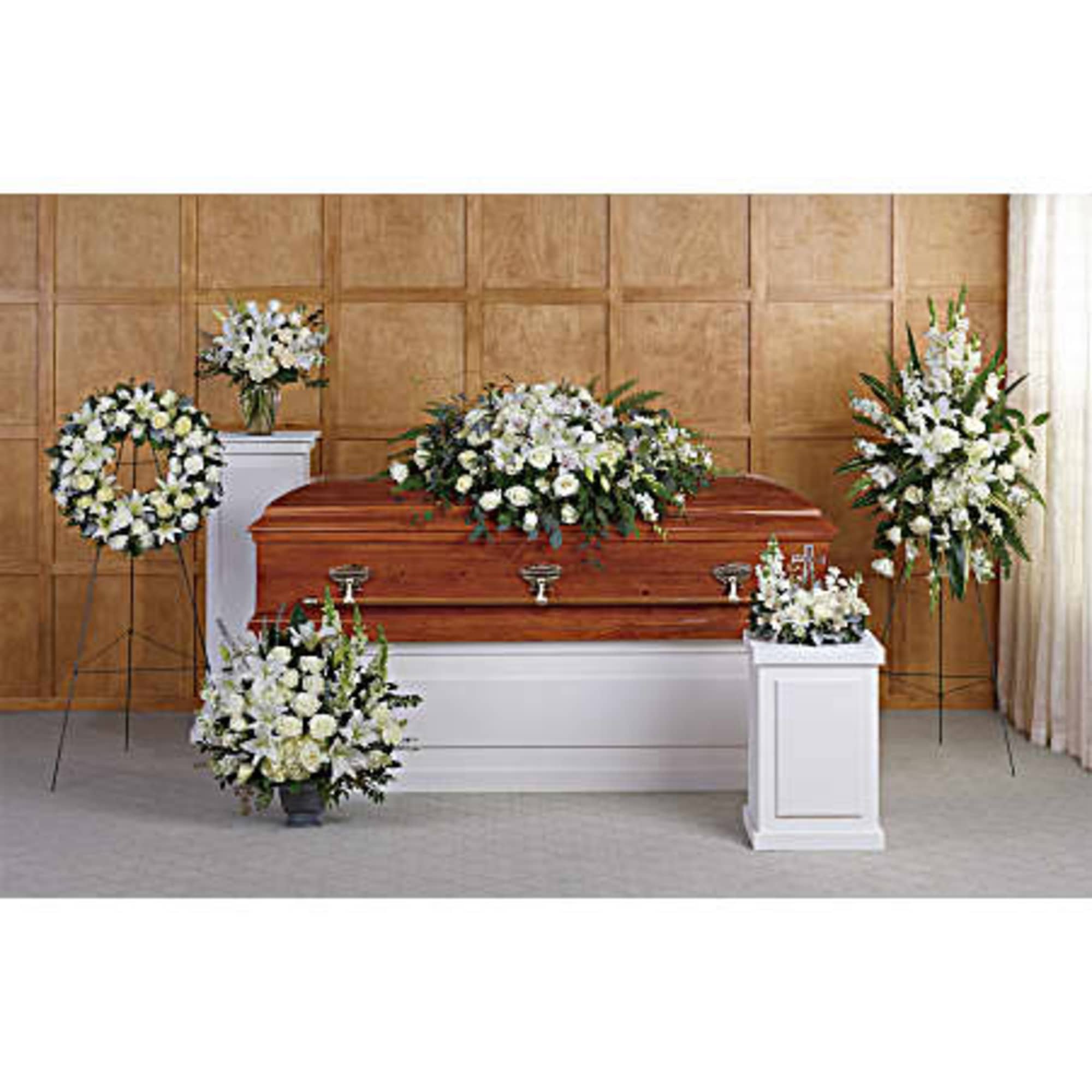 Funeral floral set with white lilies and roses arranged around a wooden casket