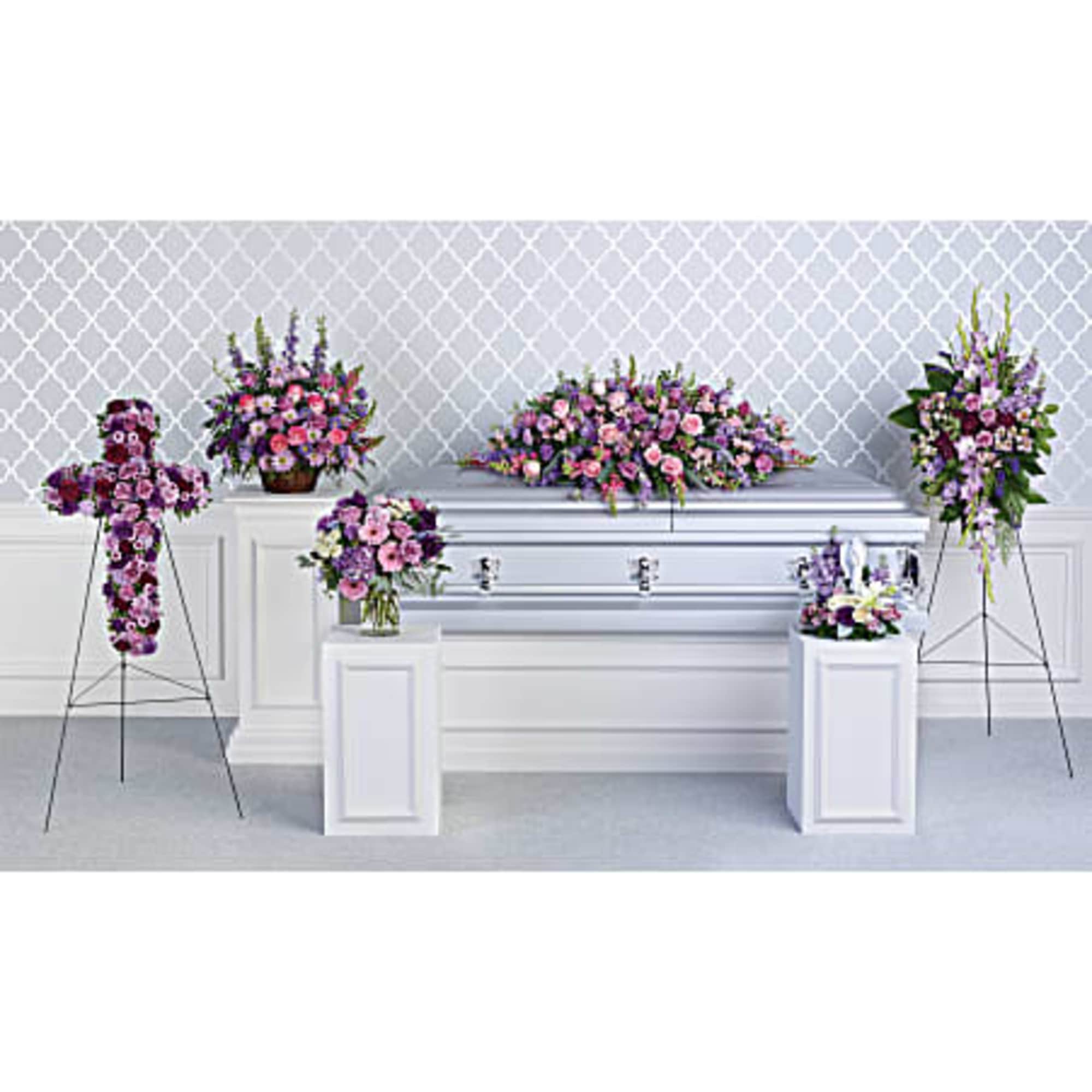 Set of pink and purple funeral arrangements surrounding a silver casket