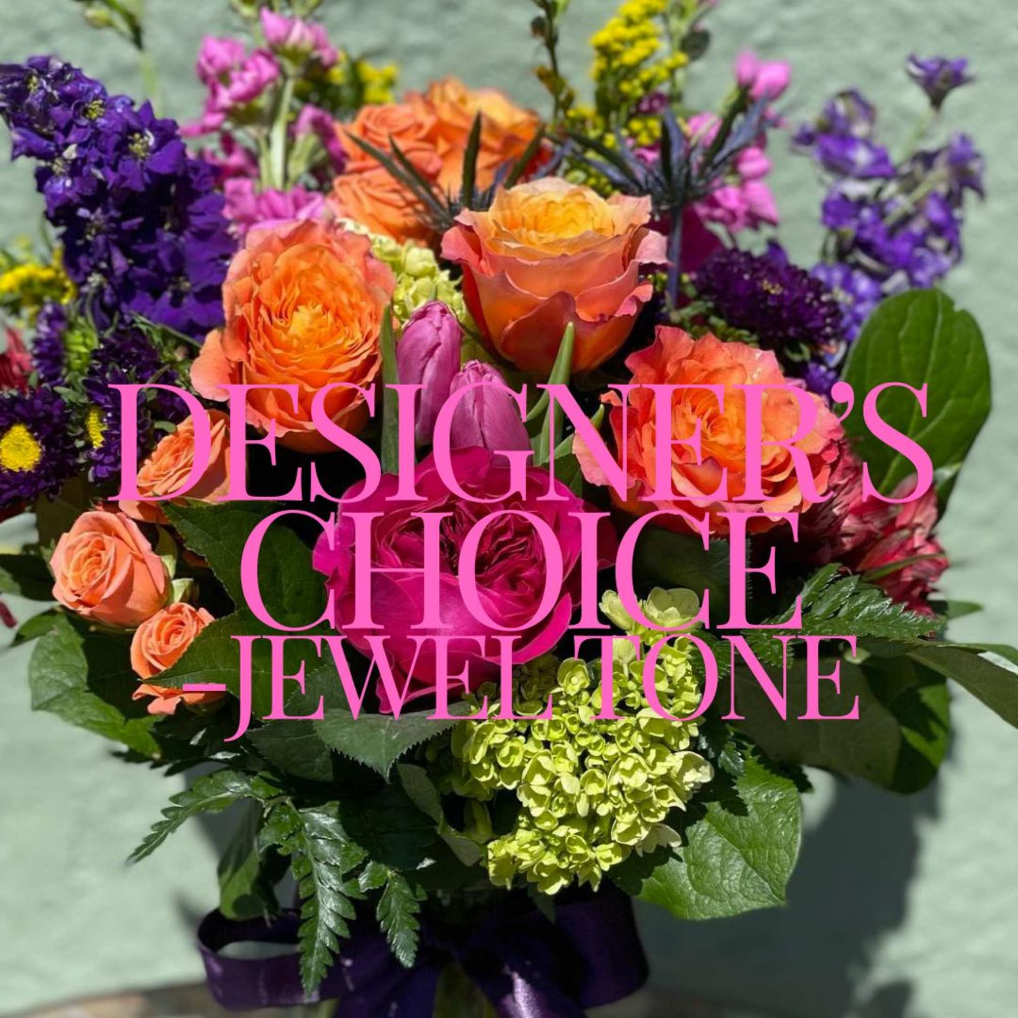 Jewel-tone bouquet of orange and pink roses with purple blooms in a glass vase
