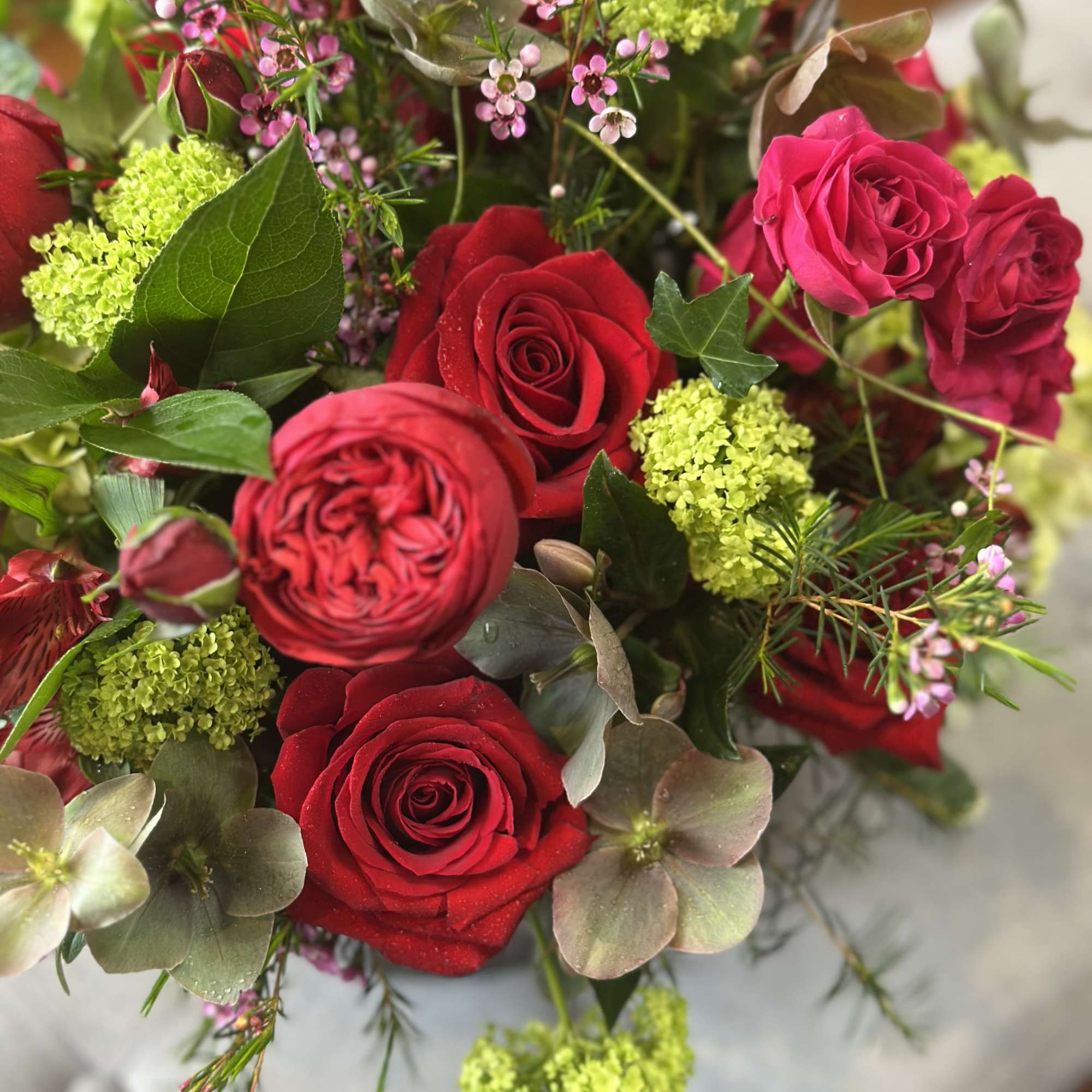 Arrangement of red and hot pink roses mixed with lime green and mauve blooms in a lush bouquet