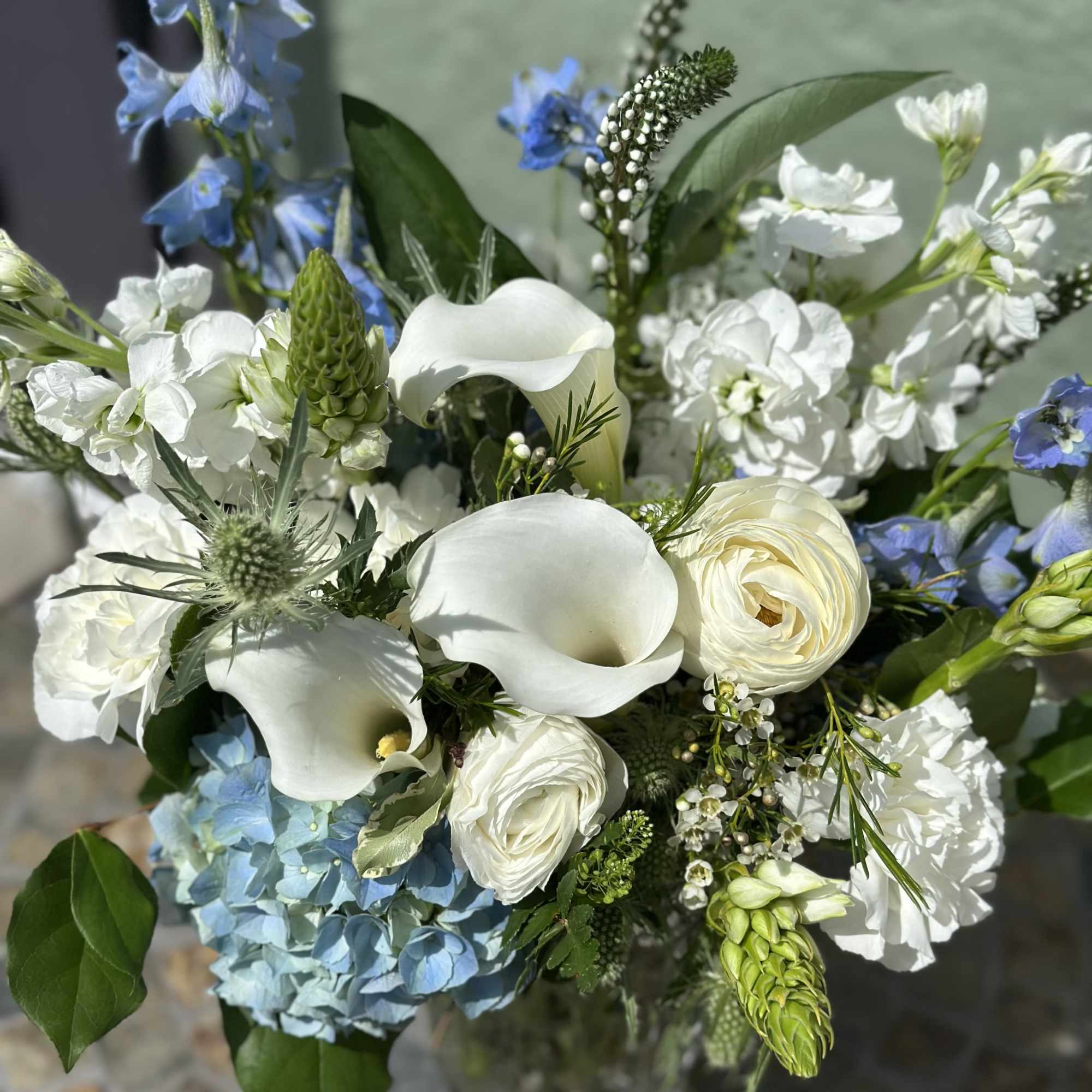 White calla lilies and roses with blue hydrangea in a clear glass vase.
