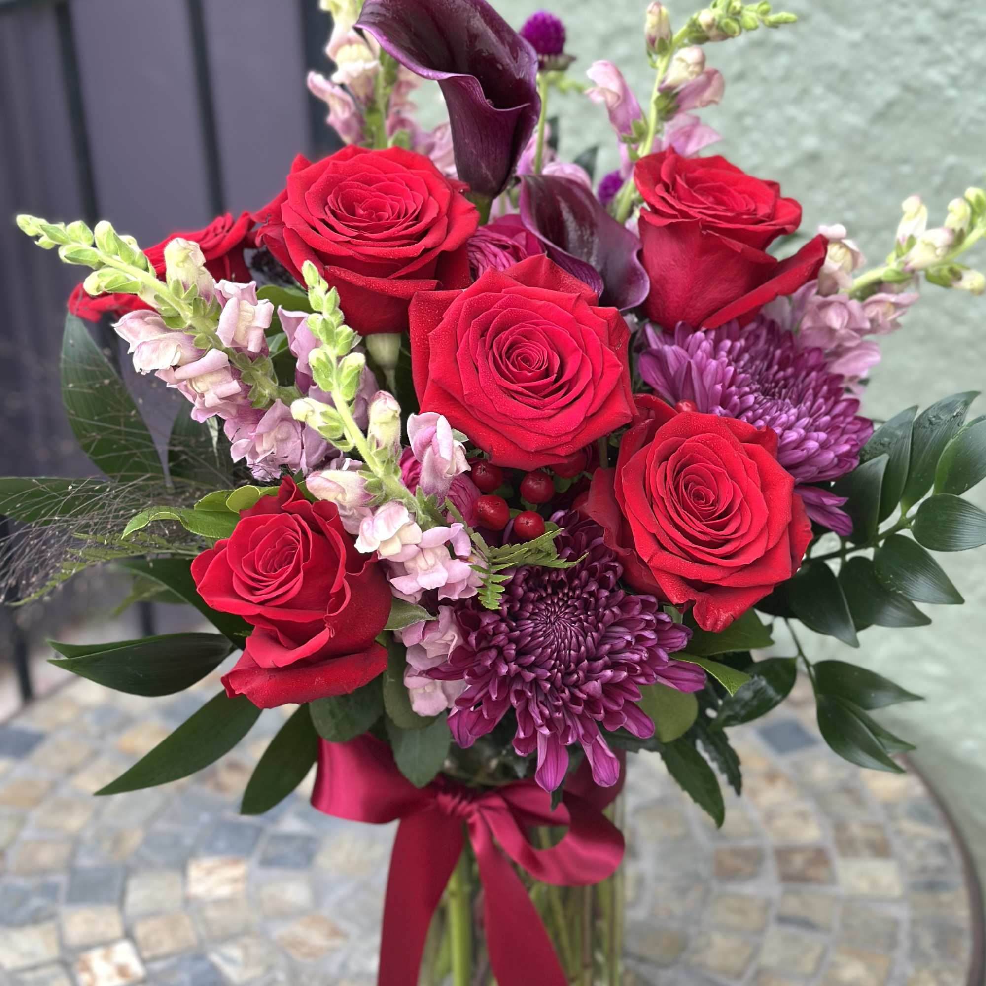 Bouquet of red roses and purple flowers in a glass vase with a ribbon