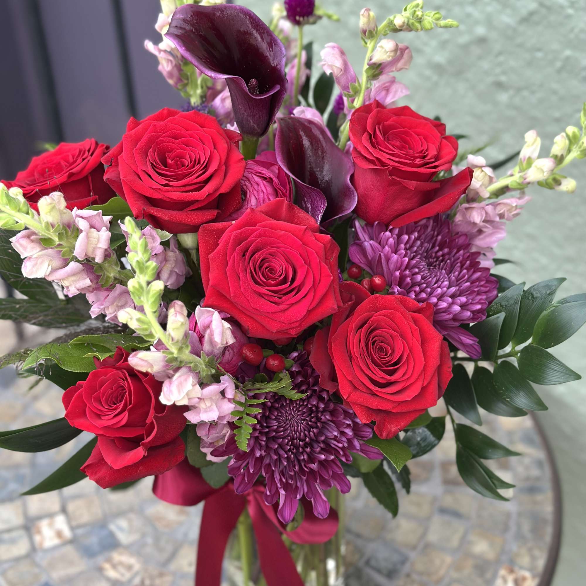 Bouquet of red roses, purple calla lilies, and pink snapdragons in a glass vase