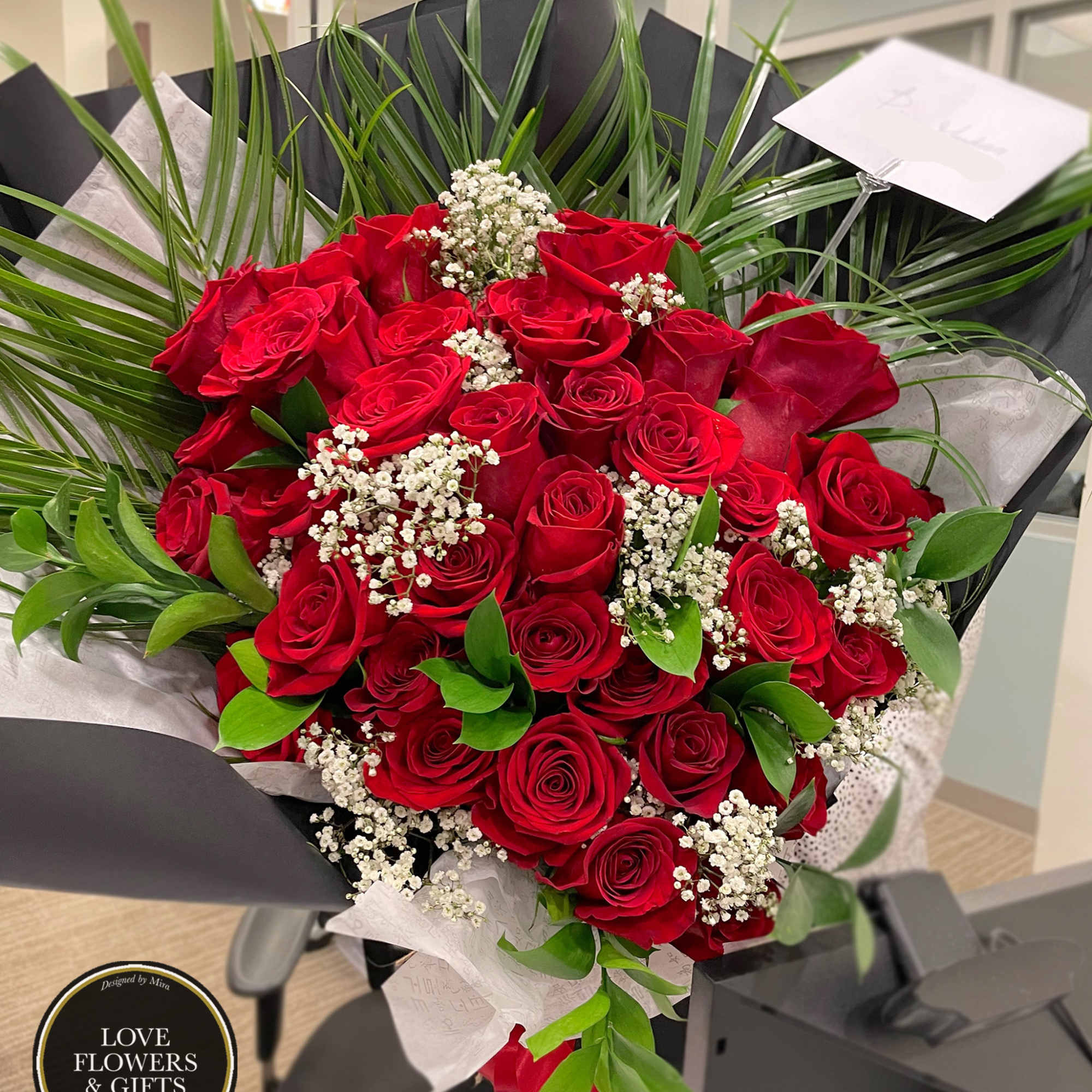 Large bouquet of red roses with white filler flowers and palm leaves wrapped in black paper