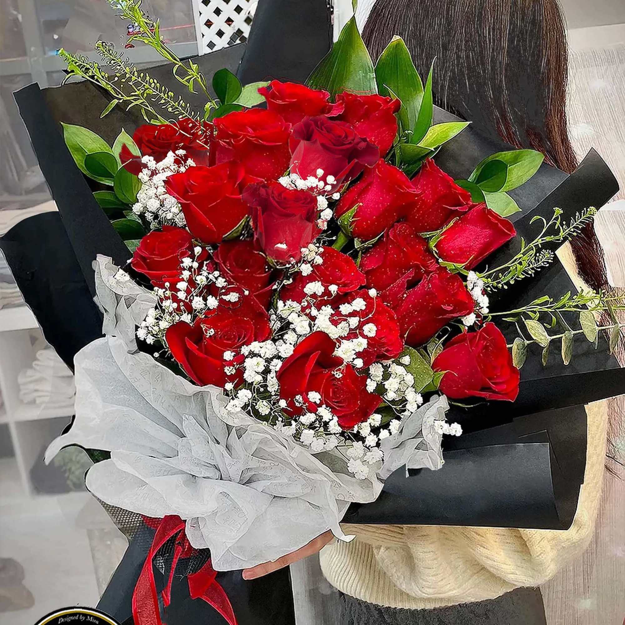Large hand-tied bouquet of red roses with white filler flowers wrapped in black paper and white tissue.