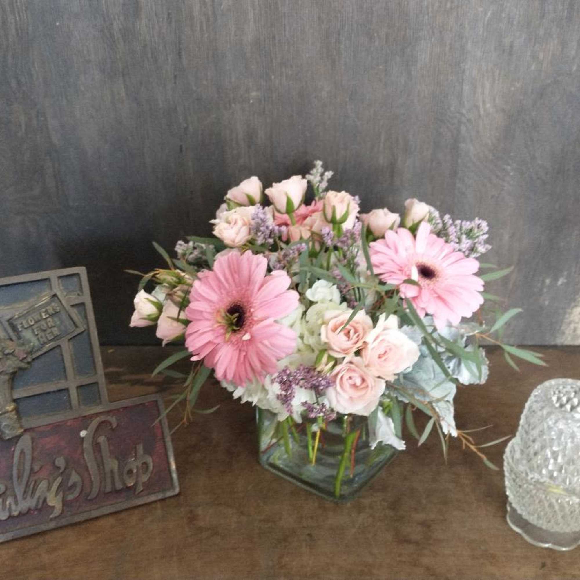 Pink gerbera daisies and roses in a square glass vase