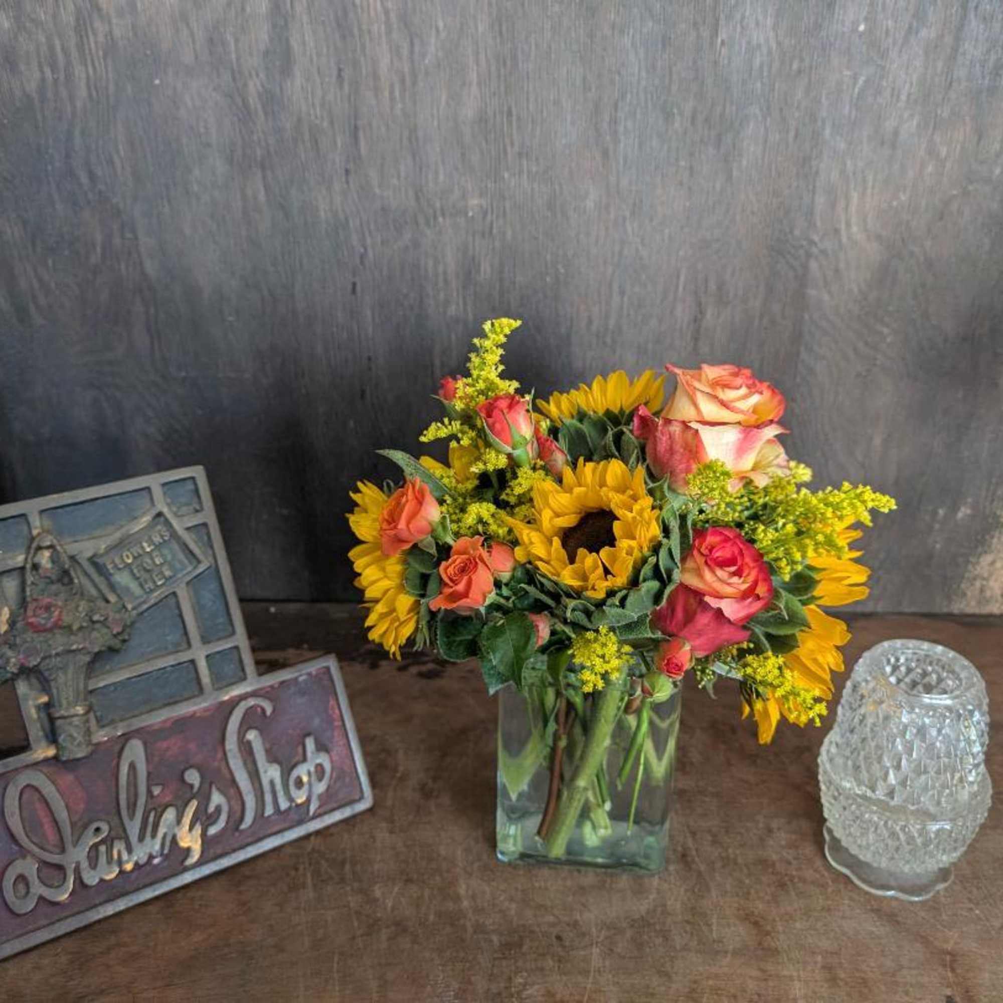 Sunflowers and peach roses arranged in a clear glass vase.