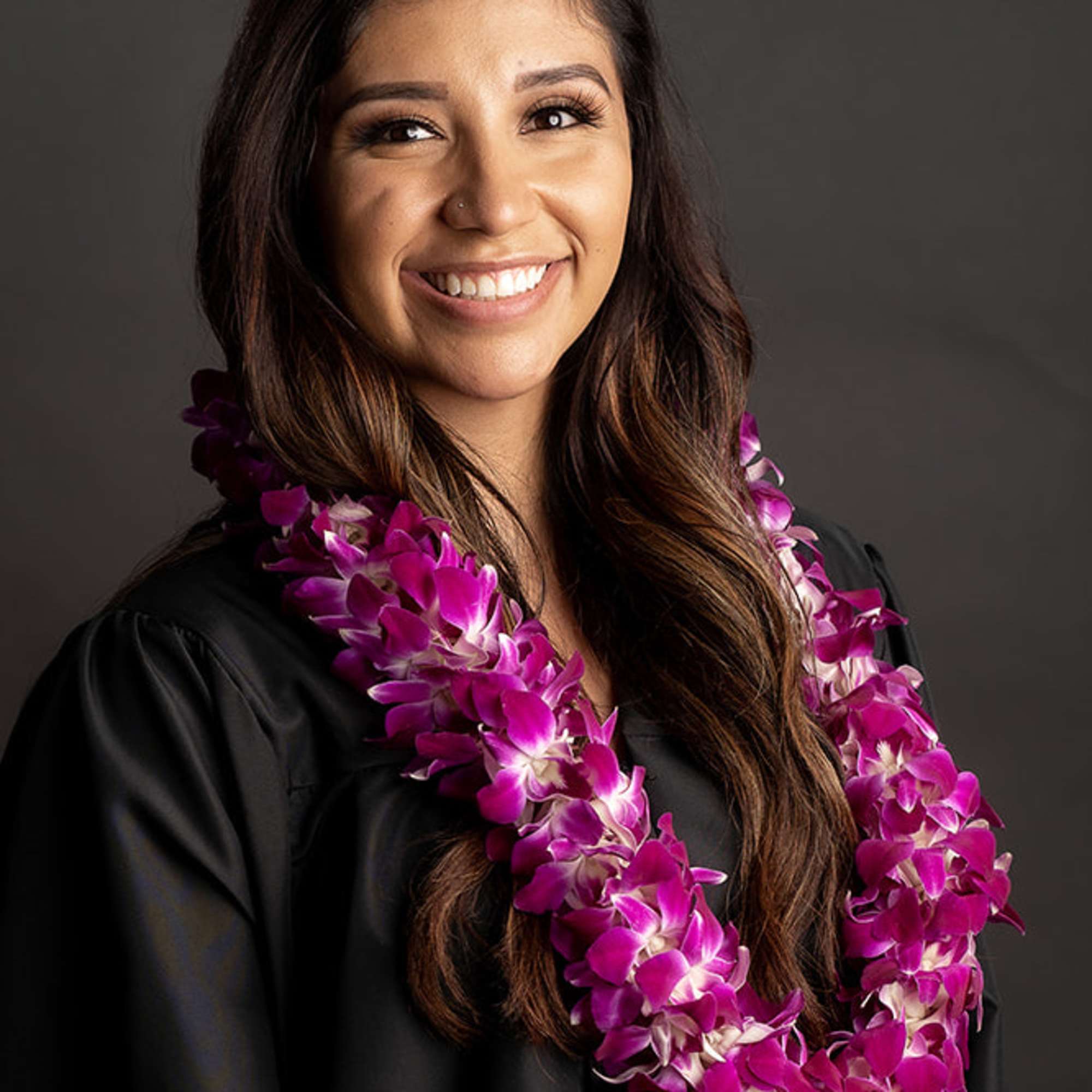 Woman wearing a purple orchid lei over a black graduation gown