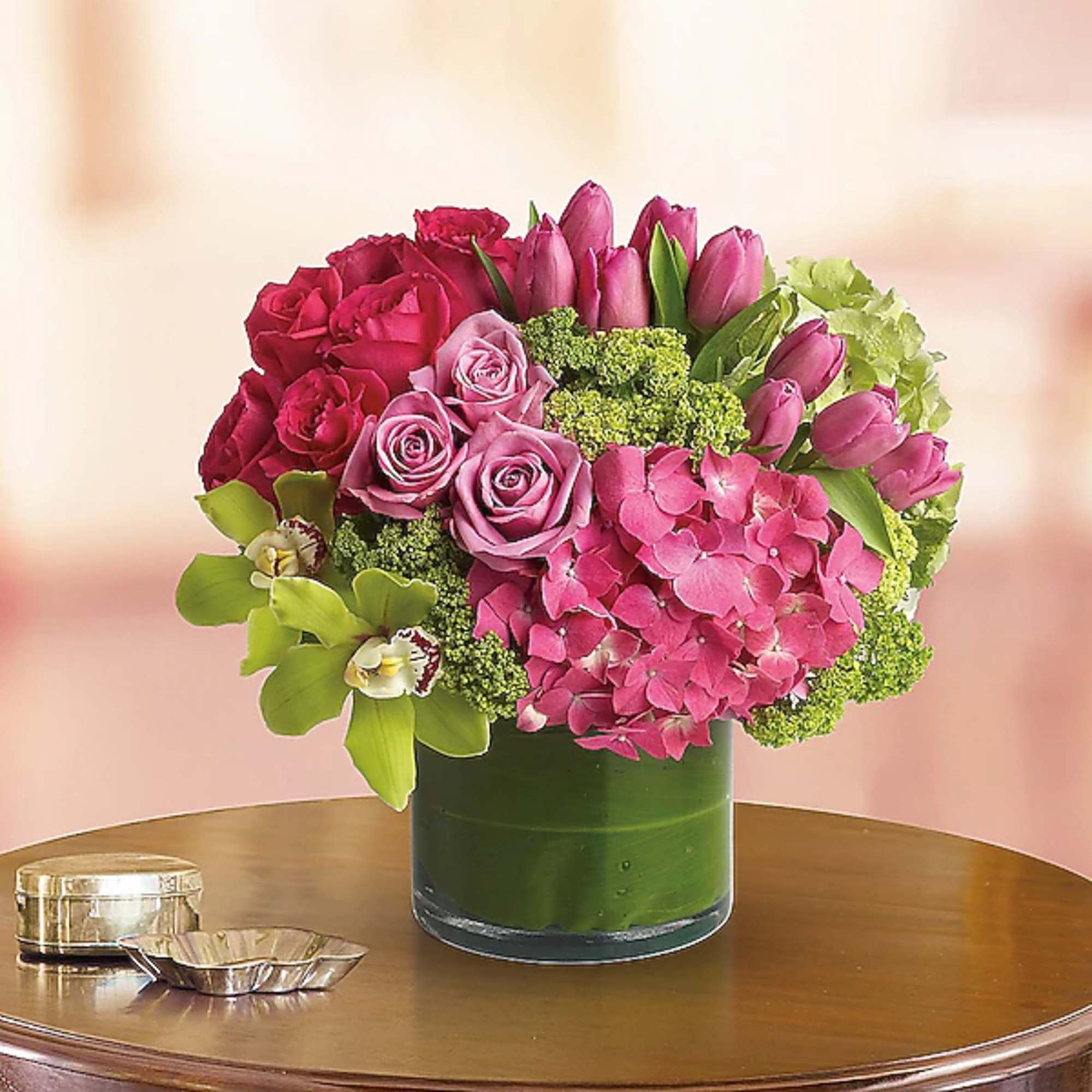 Pink roses and tulips arranged in a glass vase with green hydrangeas