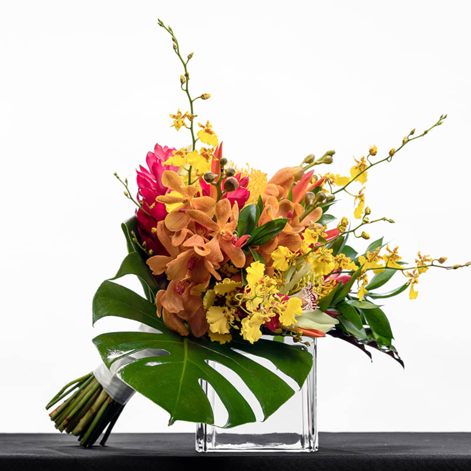 Tropical bouquet of yellow and orange orchids with pink blooms in a clear glass cube vase