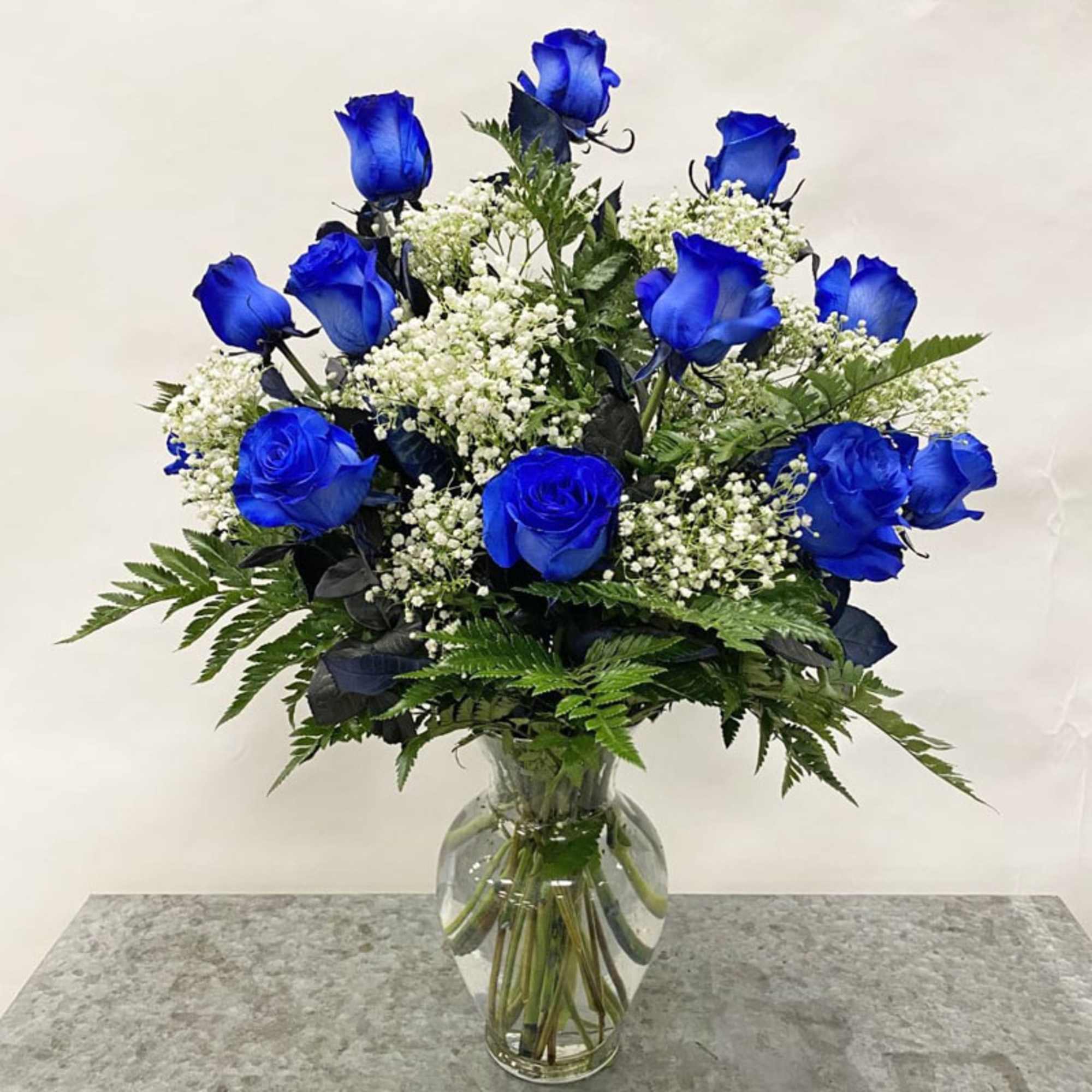 Vase arrangement of vivid blue roses with white filler flowers in a clear glass vase