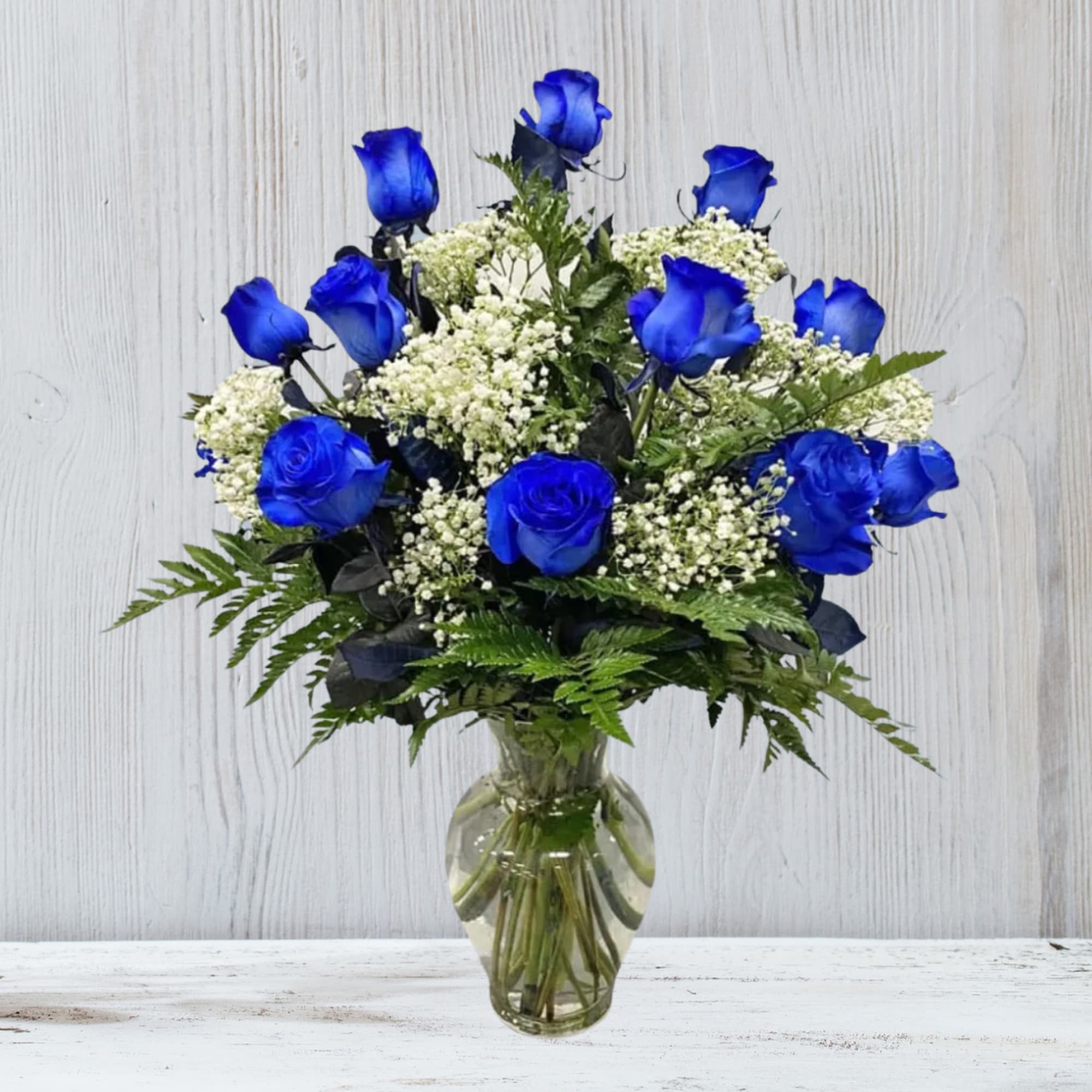 Arrangement of vivid blue roses with white filler flowers in a clear glass vase