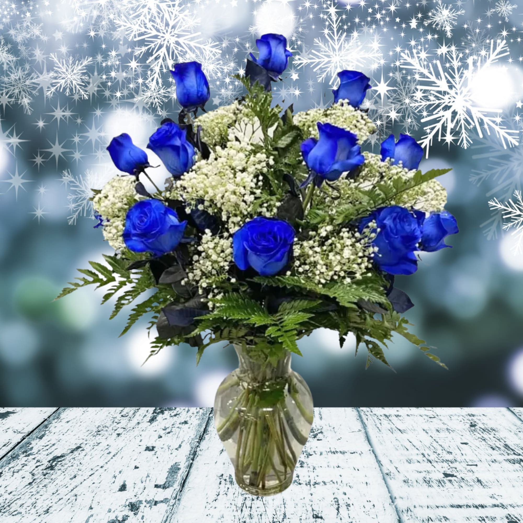 Arrangement of bright blue roses and white filler flowers in a clear glass vase on a rustic wood surface